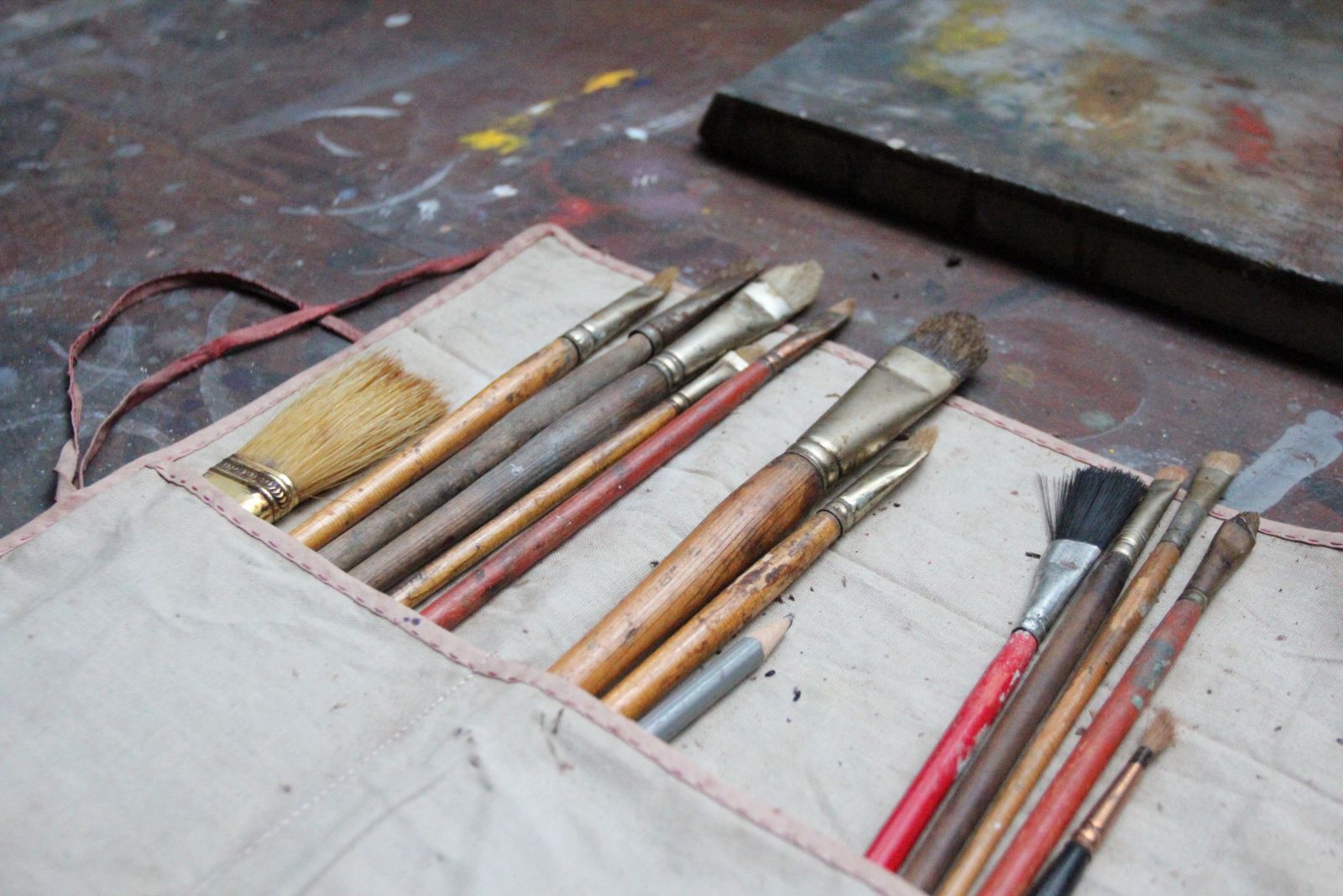 Old paintbrushes covered in small splatters of paint rest on a table