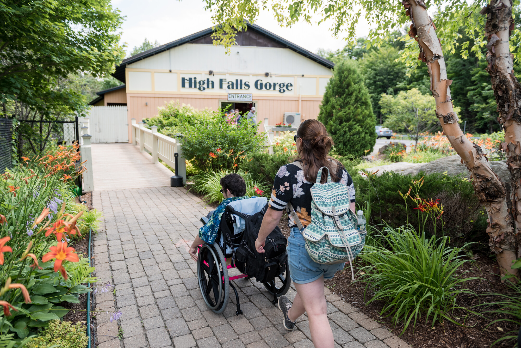 A person follows behind another person in a wheelchair on the walkway towards high falls gorge