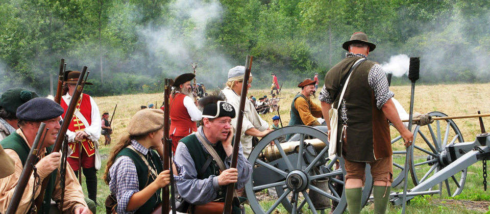 An array of costumed reenactors participate in a mock battle.