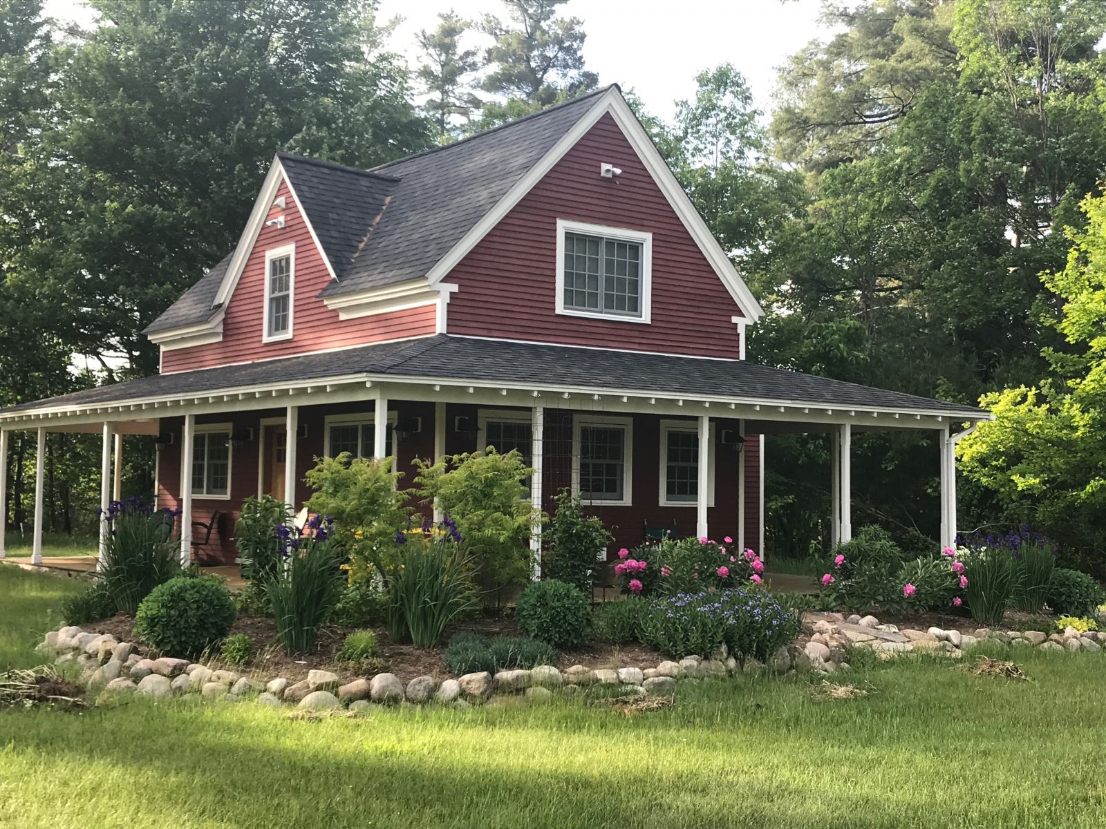 A red house with white trim stands on a lawn while surrounded by purple flowers