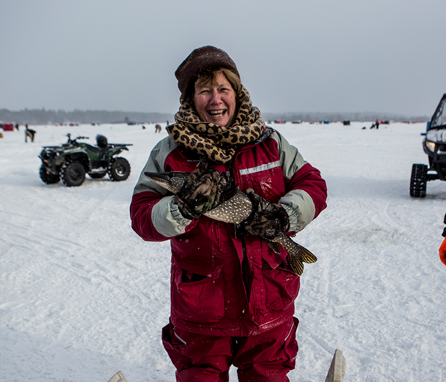 A women holds a large northern pike while out on the ice