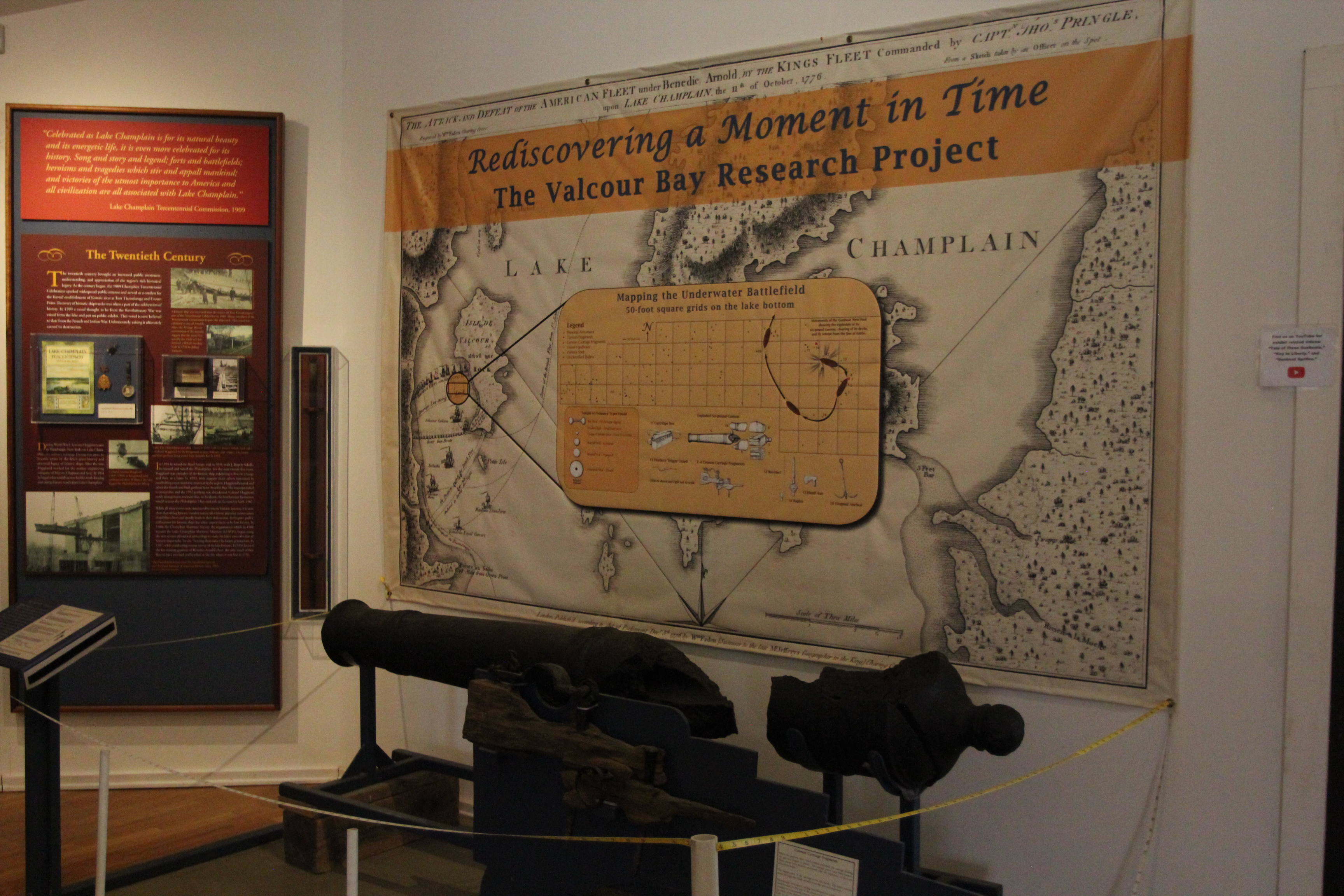 A museum exhibit displays a cannon on the remains of a wooden gun carriage with large informational signs. 