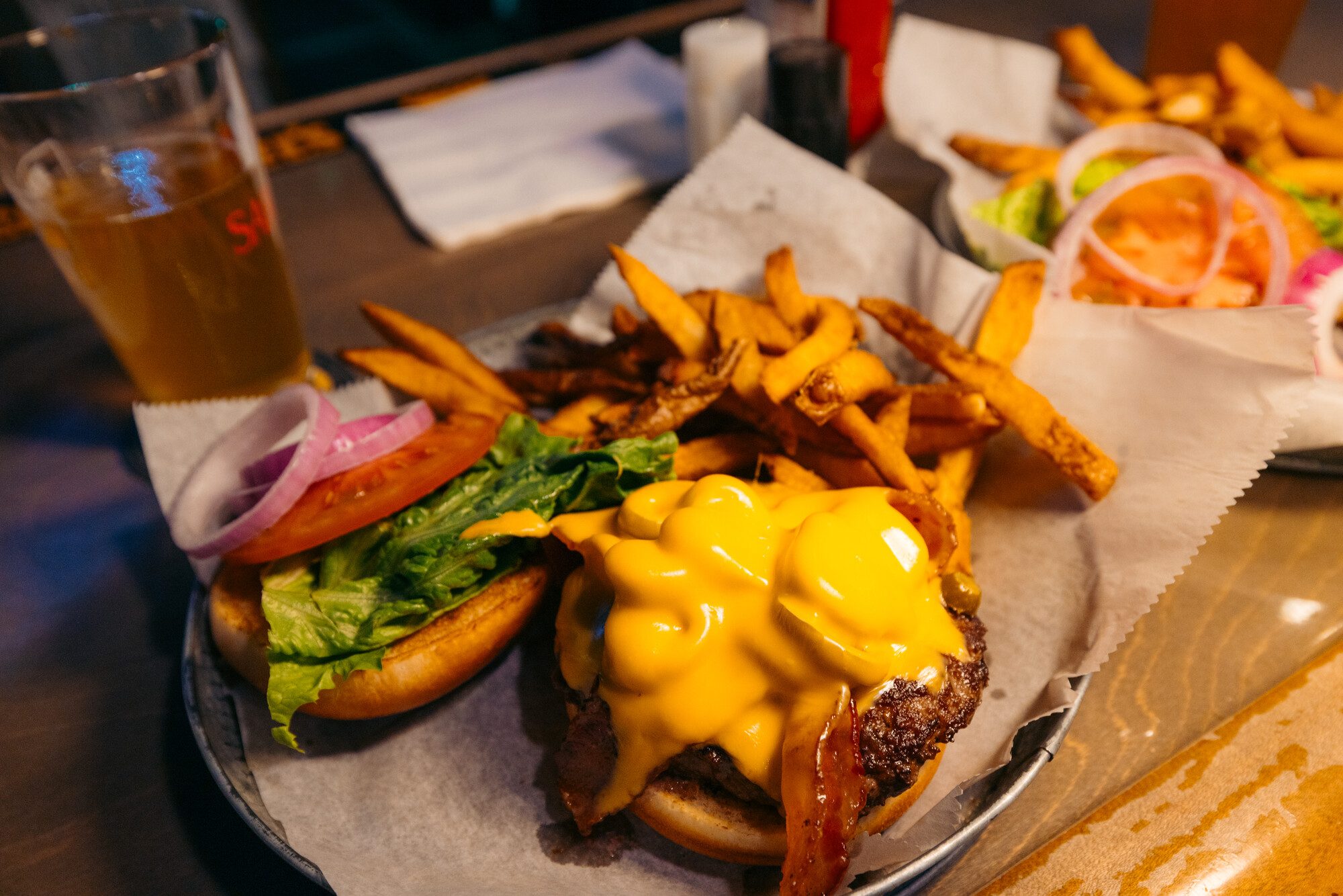 A cheeseburger, fries and a brew sits on a table at Twisted Raven 
