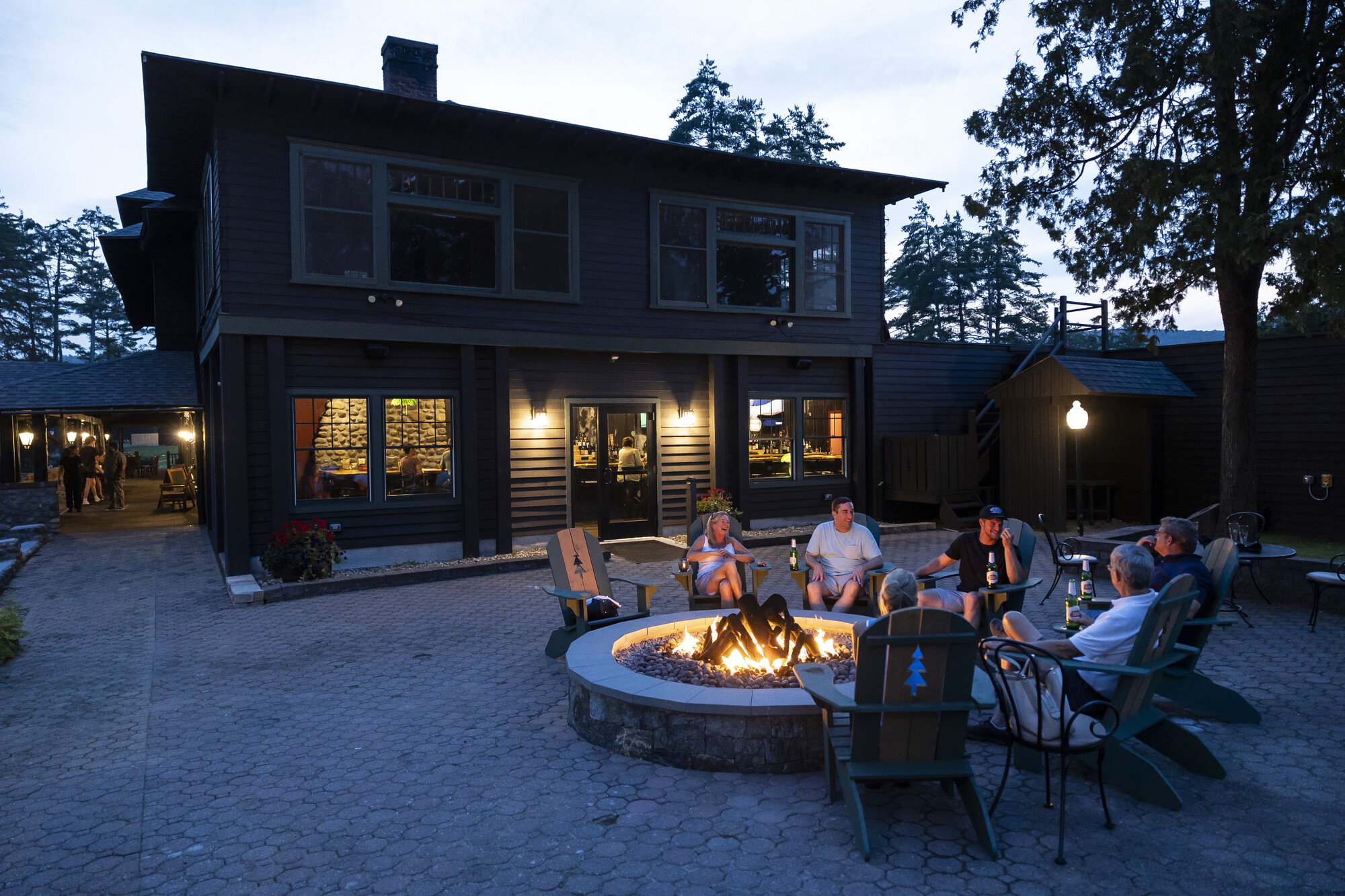 A group of friends laugh together in the evening on a stone patio of a lodge restaurant.