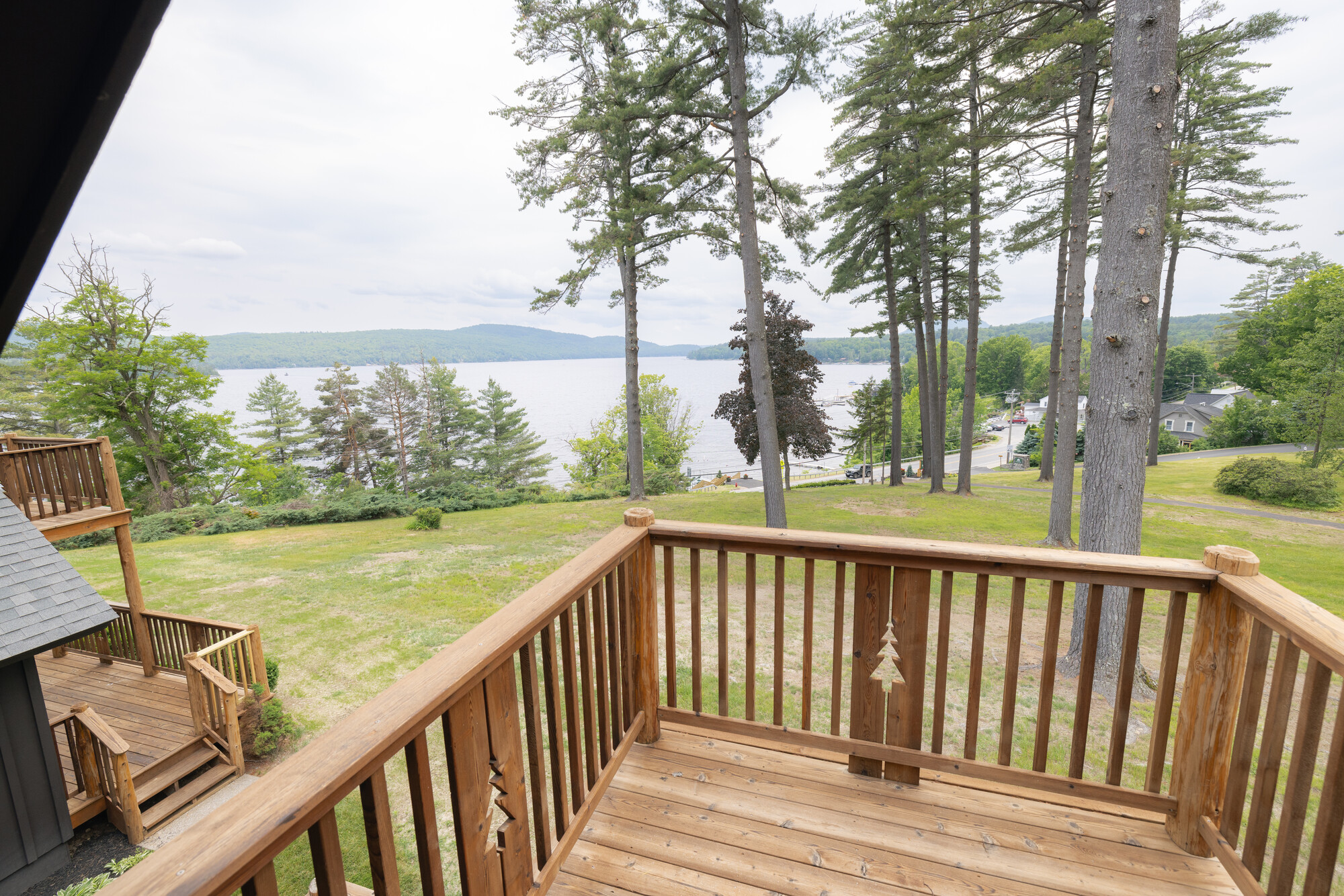 A wooden deck looks out over a tree-ringed grassy lawn, with a lake beyond.