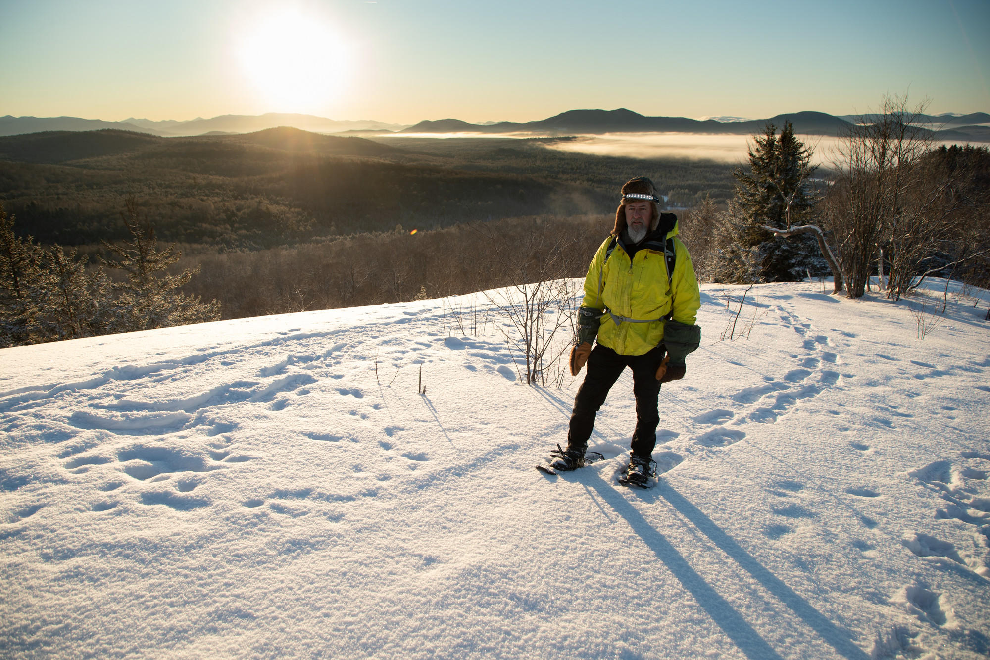 A man in a yellow jacket stands on top of a mountain in winter during sunrise 