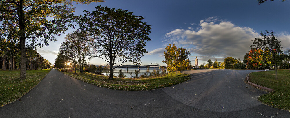 Trees align a road along a lake as red, yellow, and orange leaves begin to show