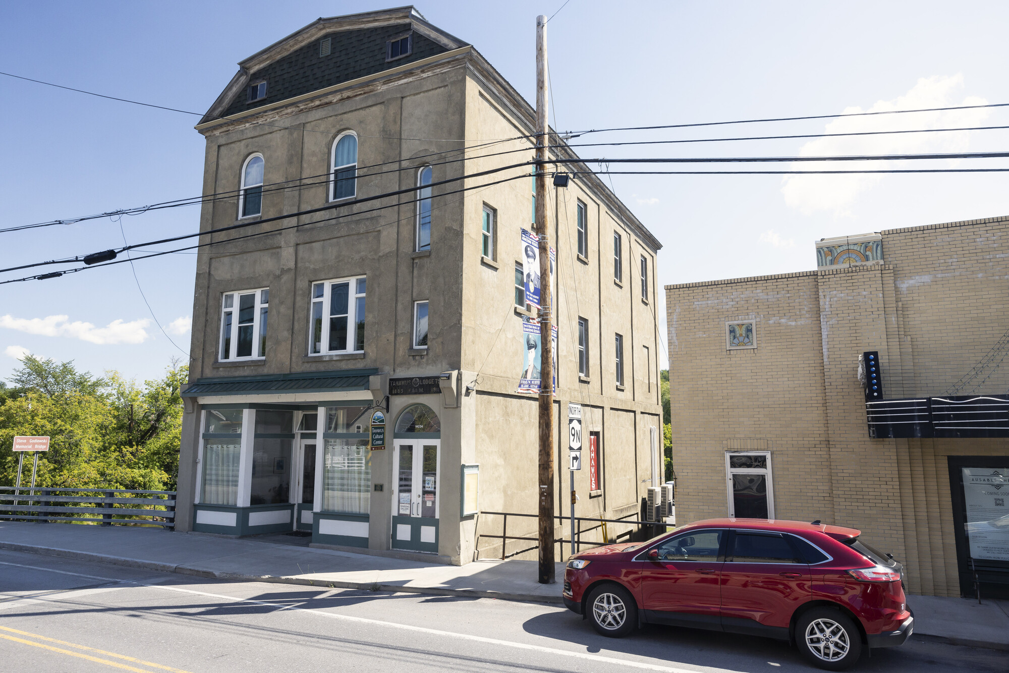 The Tahawus Center as seen from main street. A red SUV is parked out front and to the right is an old movie theater. 