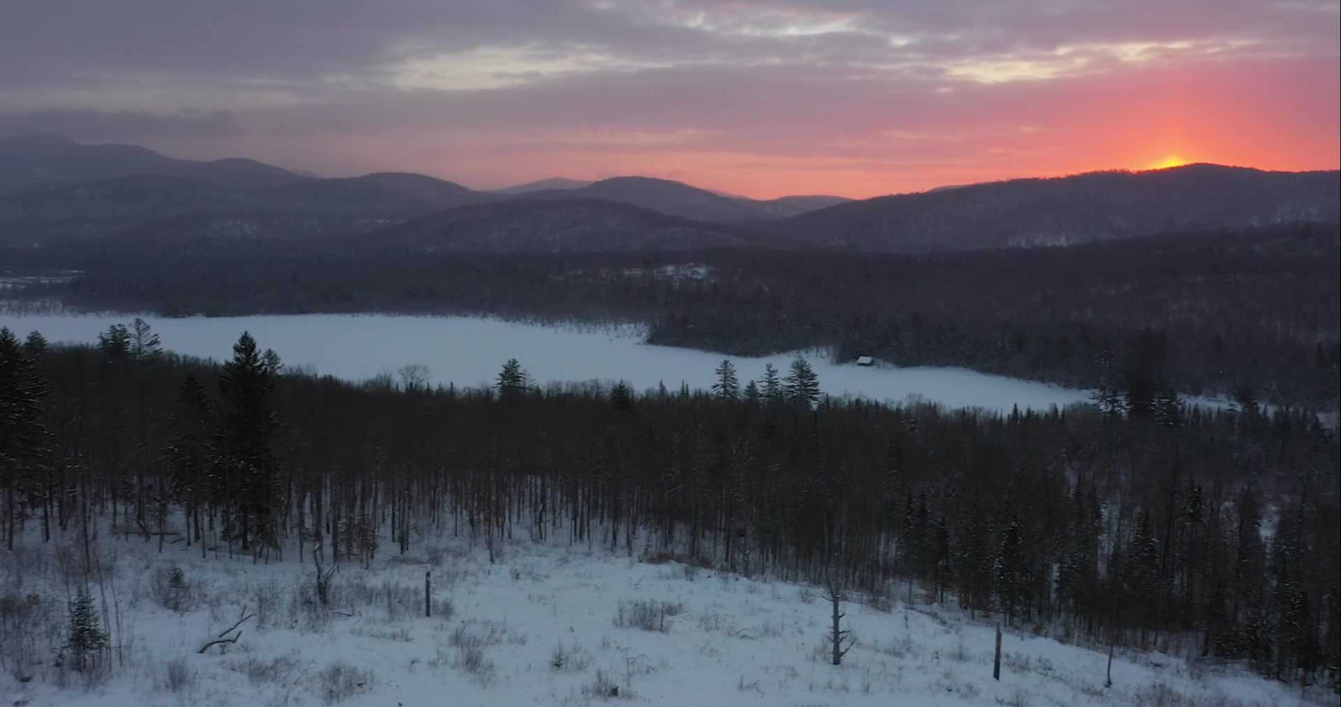 The sun rises over mountains and a snowy section of the forest