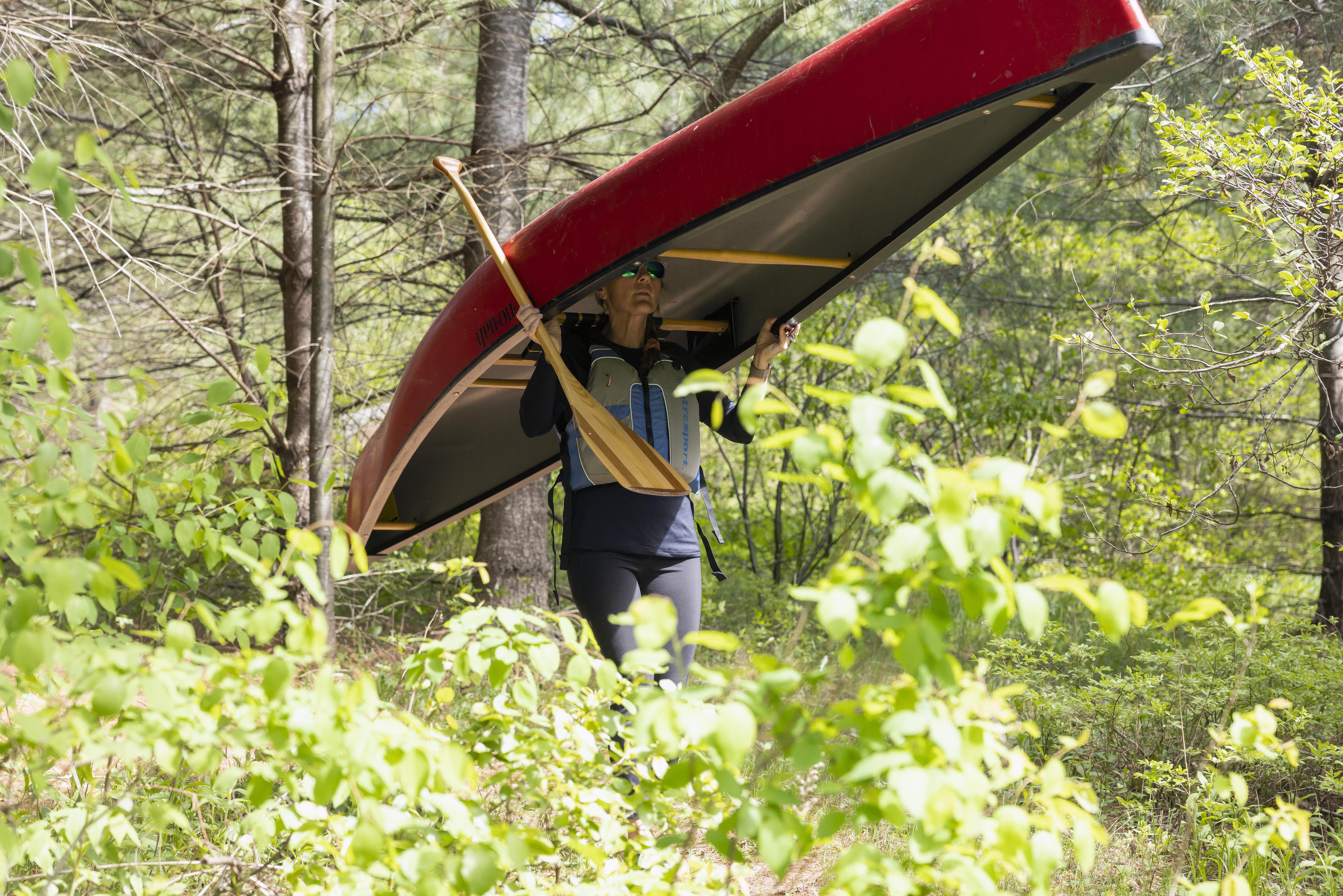 Woman carries gear, including canoe, to the lake