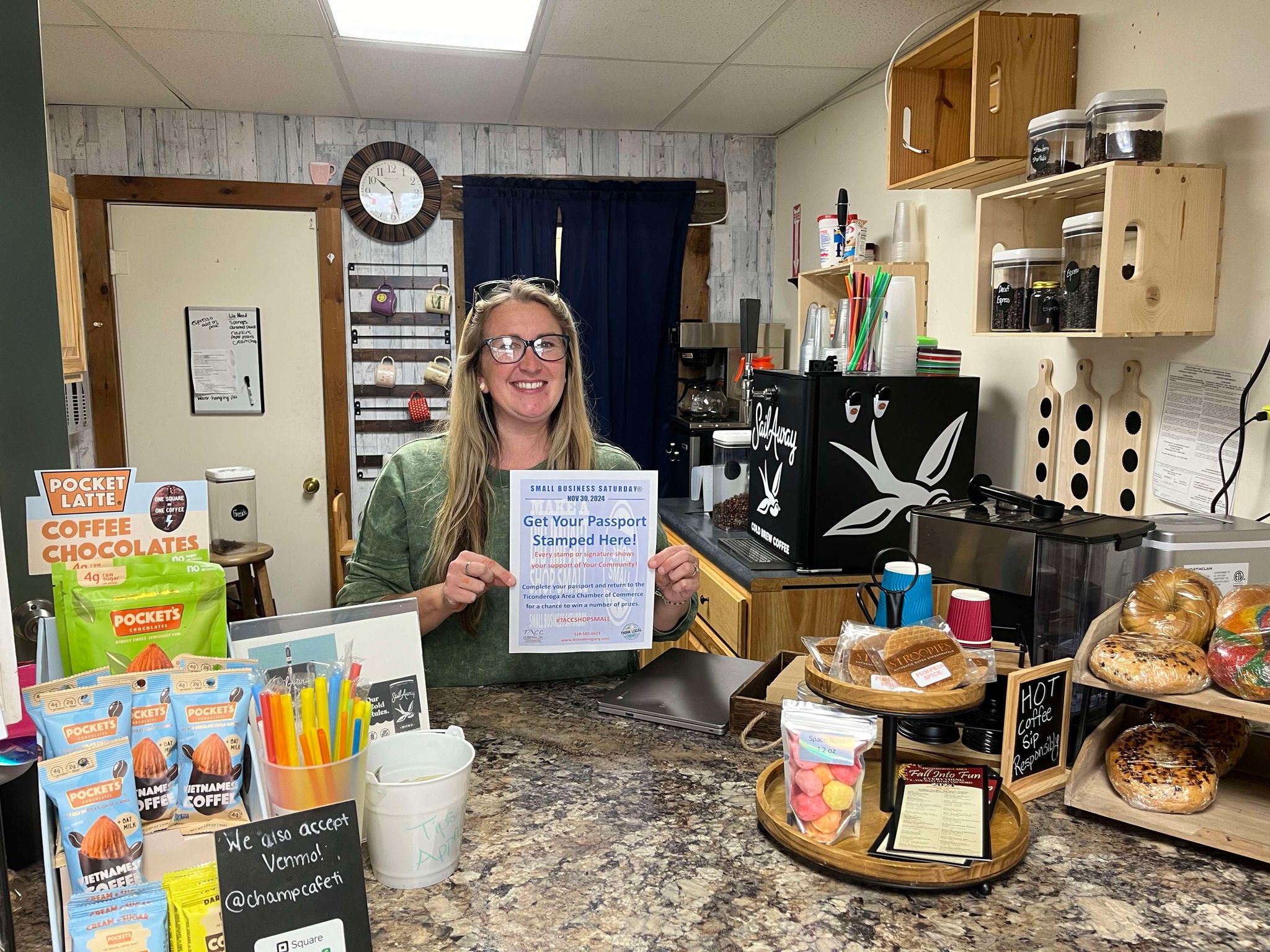 A store owner holds up a sign that says "Get You Passport Stamped Here!"