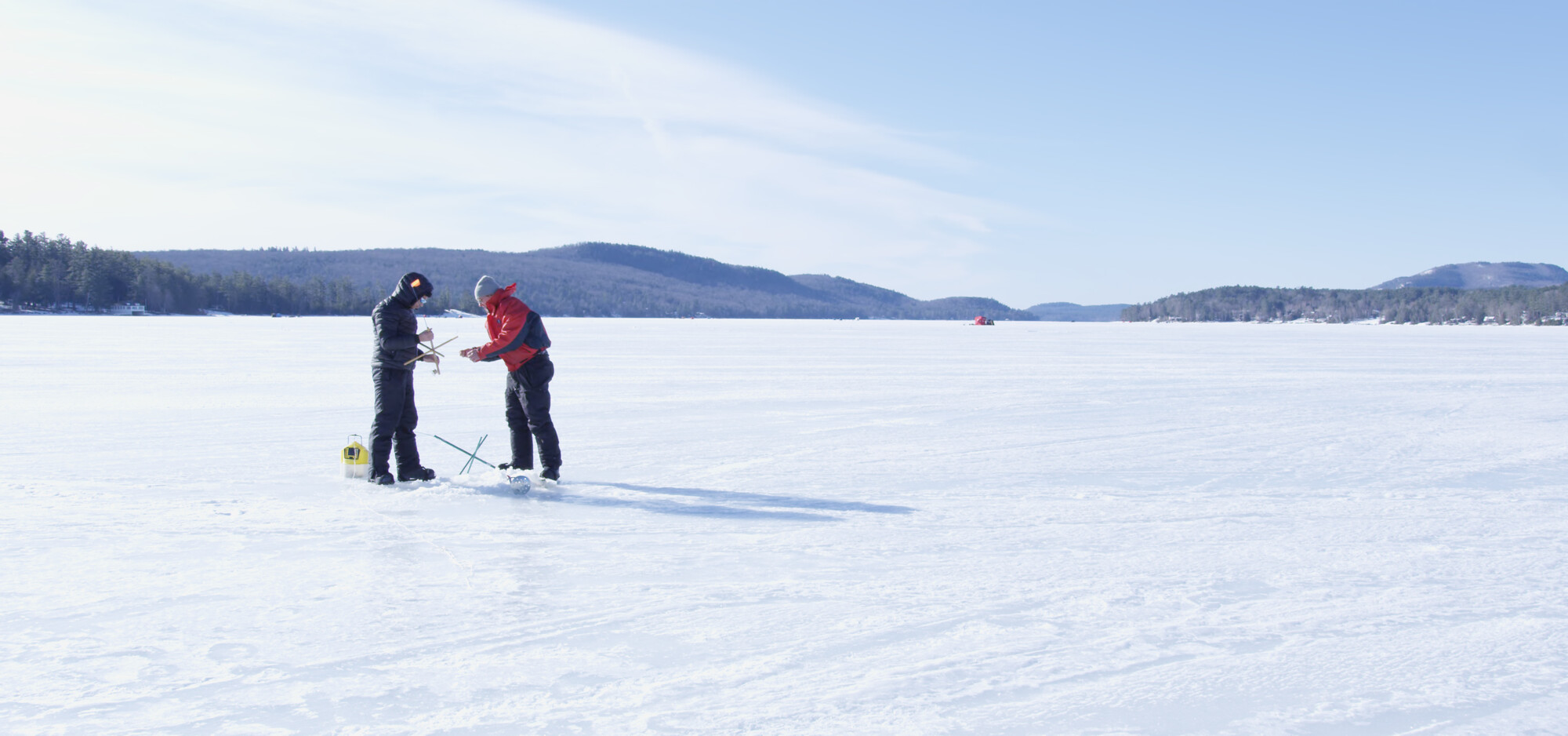 A couple ice fishers on a frozen lake amongst the mountains