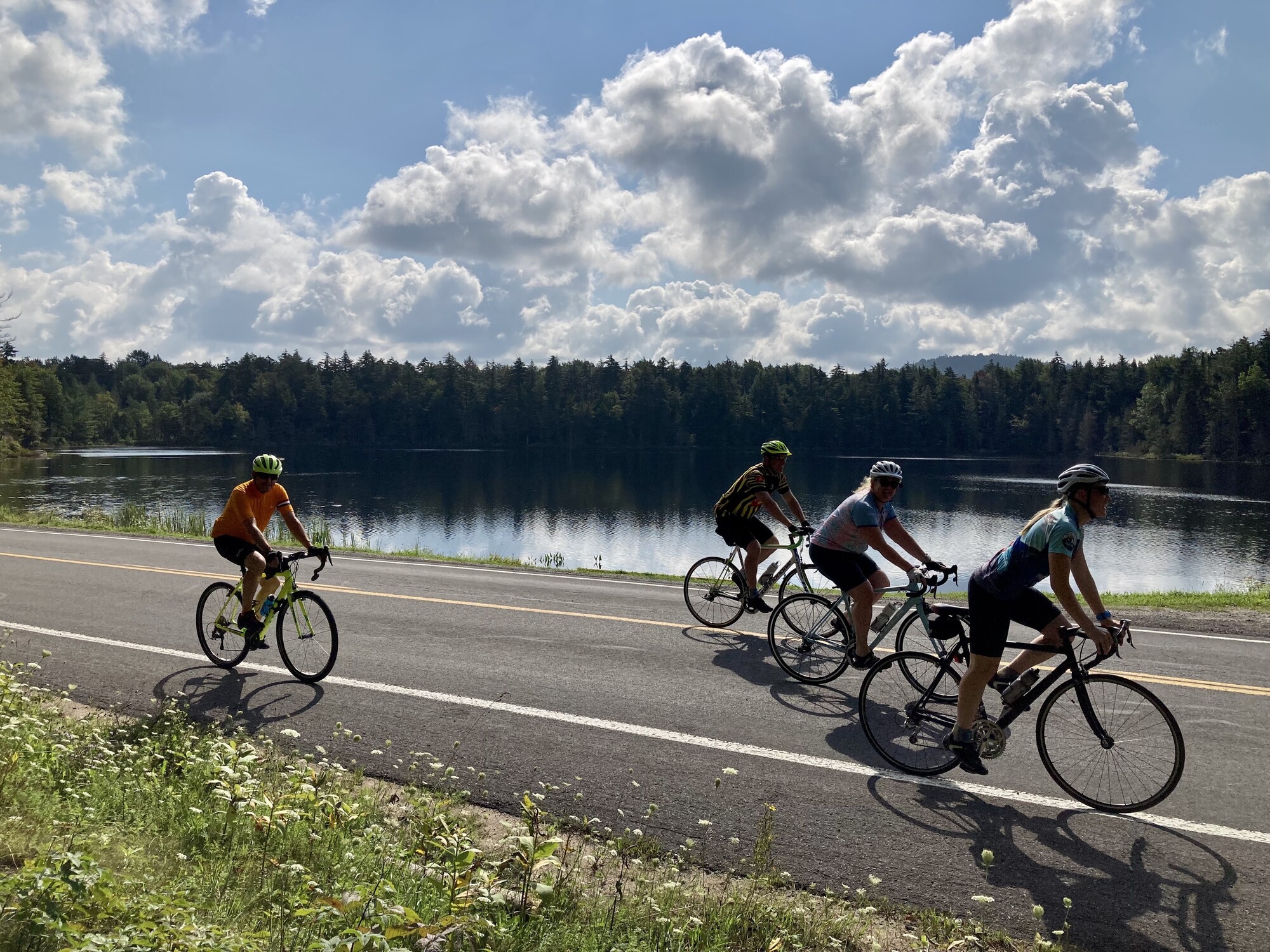 A group of people ride down a road next to a pond.