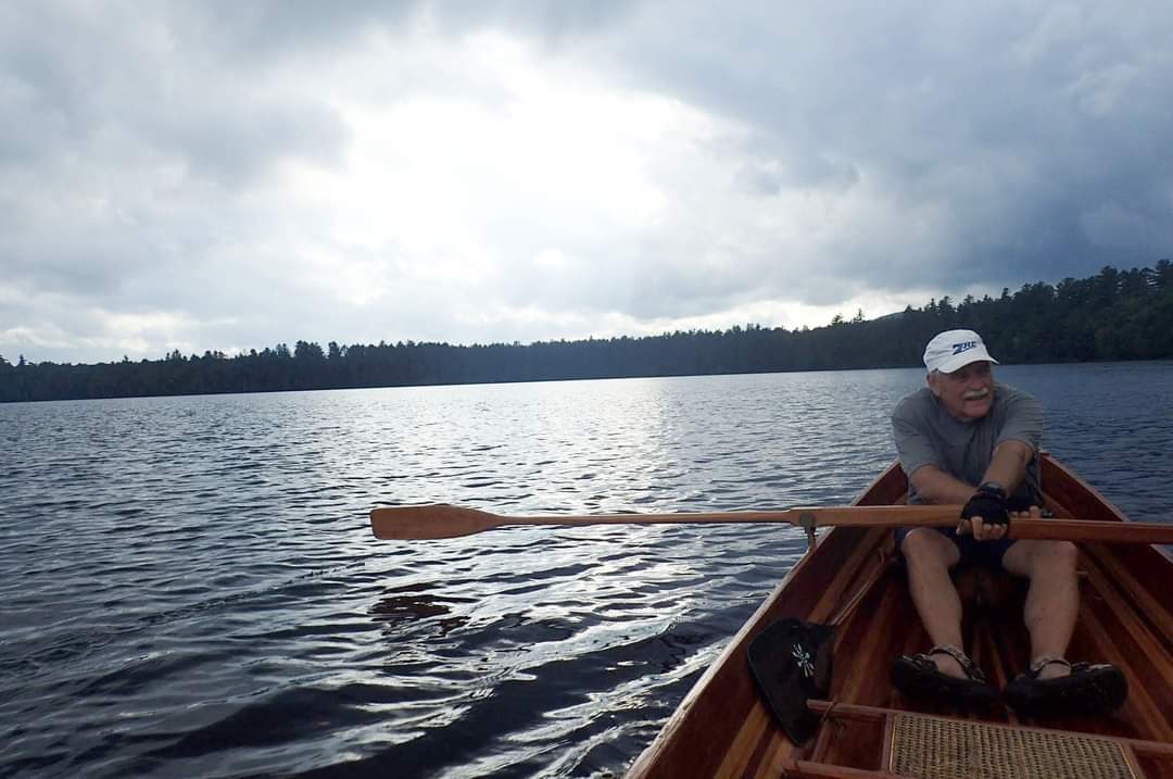 A man rows a guideboat in a lake.