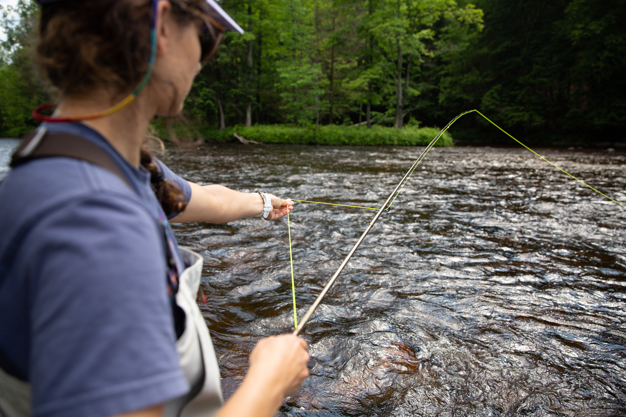 A woman guides a fly fishing rod in a river on a sunny day.