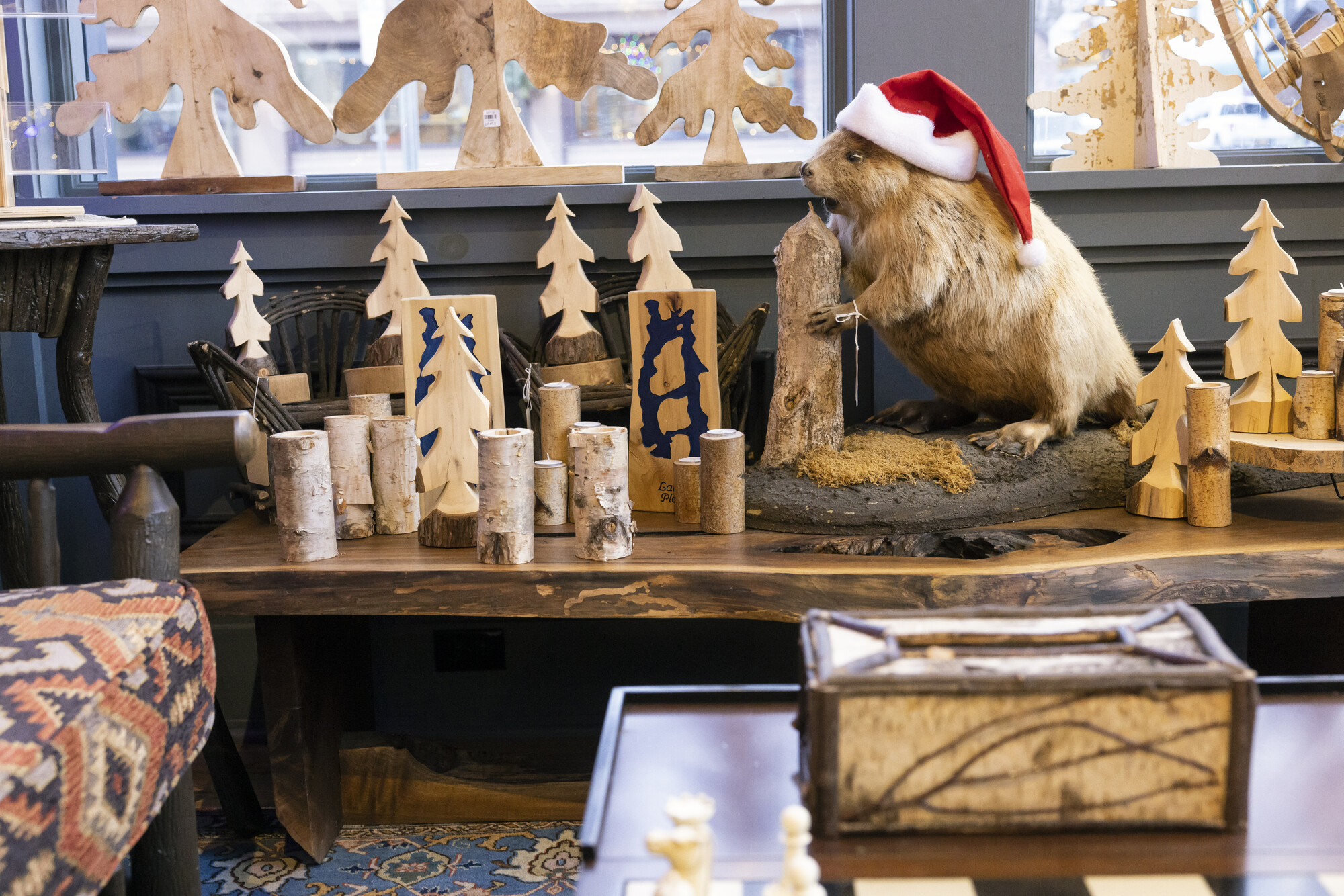 A beaver next to wooden carved trees on a display.