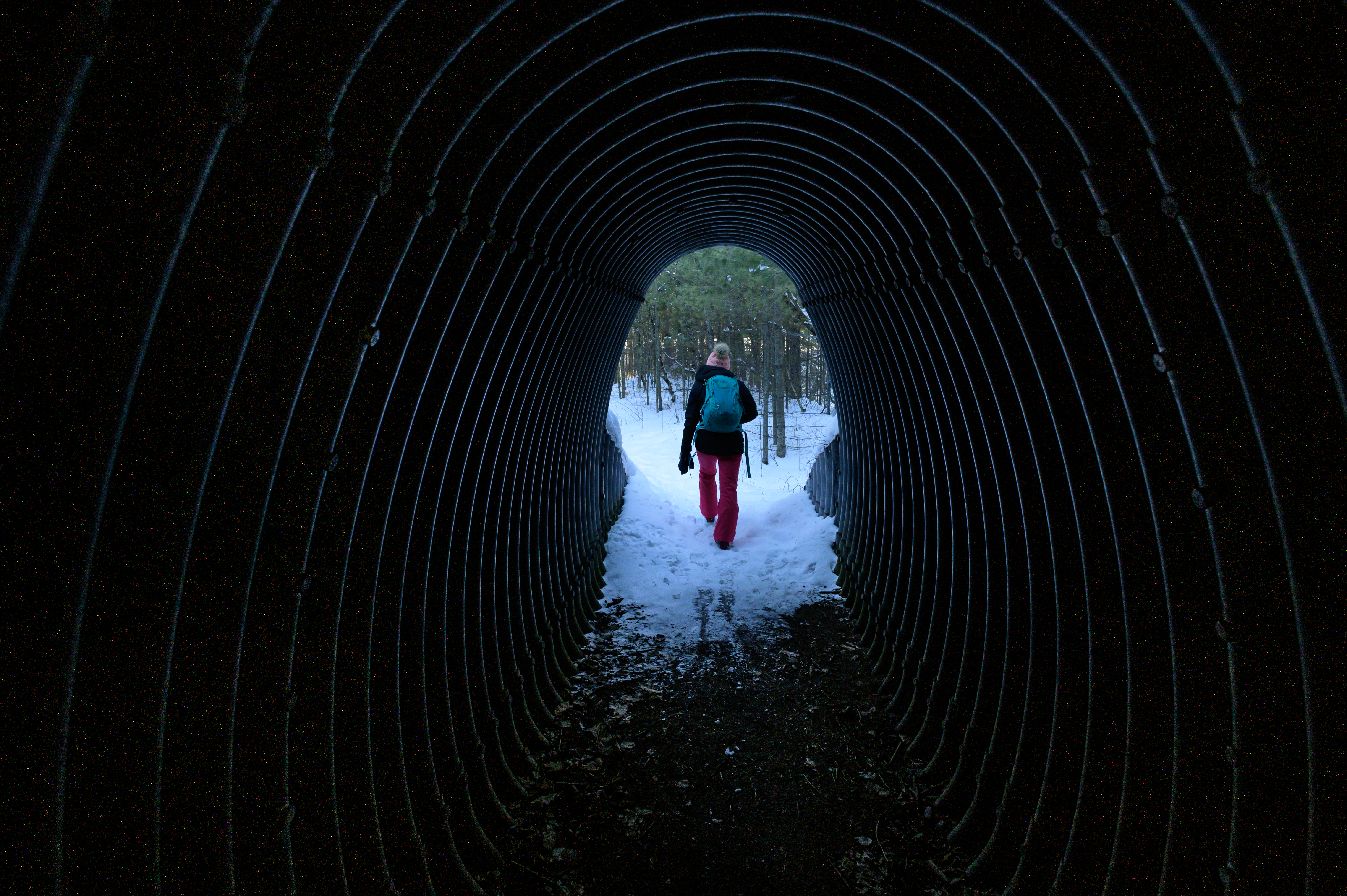Woman walking through tunnel under a highway.