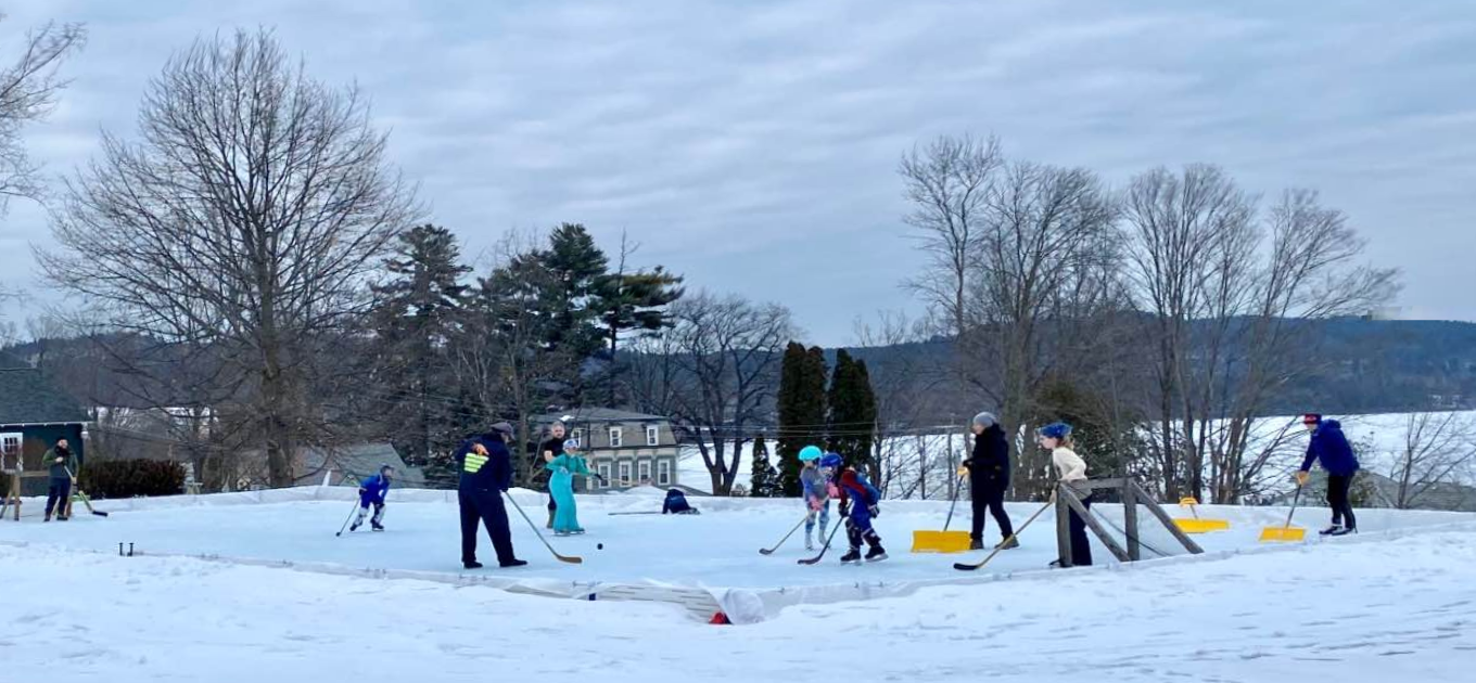 Children and adults play on an ice skating rink in winter.