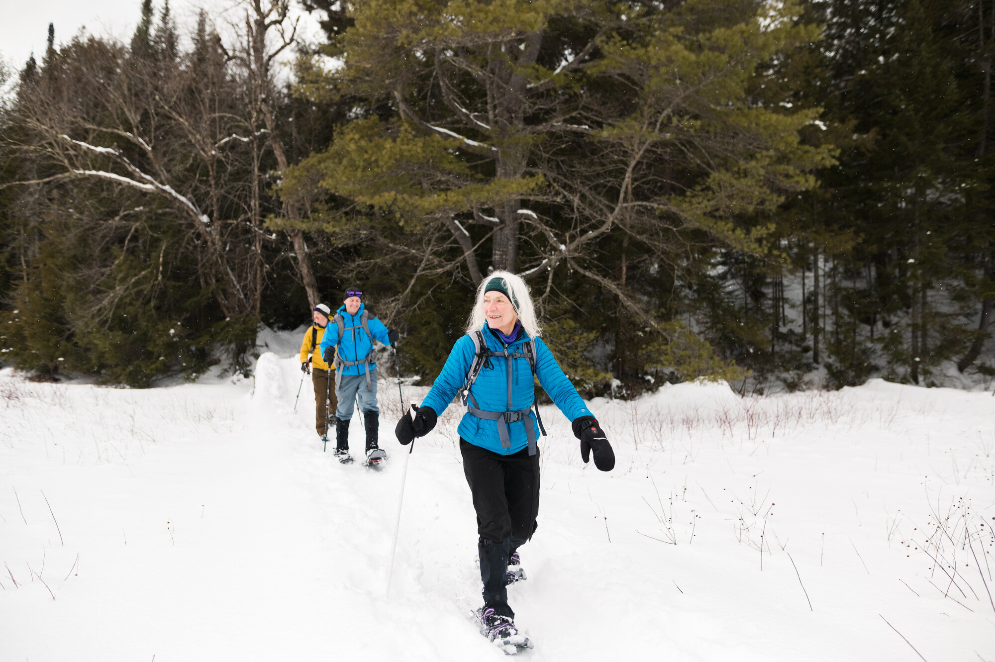 A trio walks on a snoeshoe path after crossing a bridge in snow