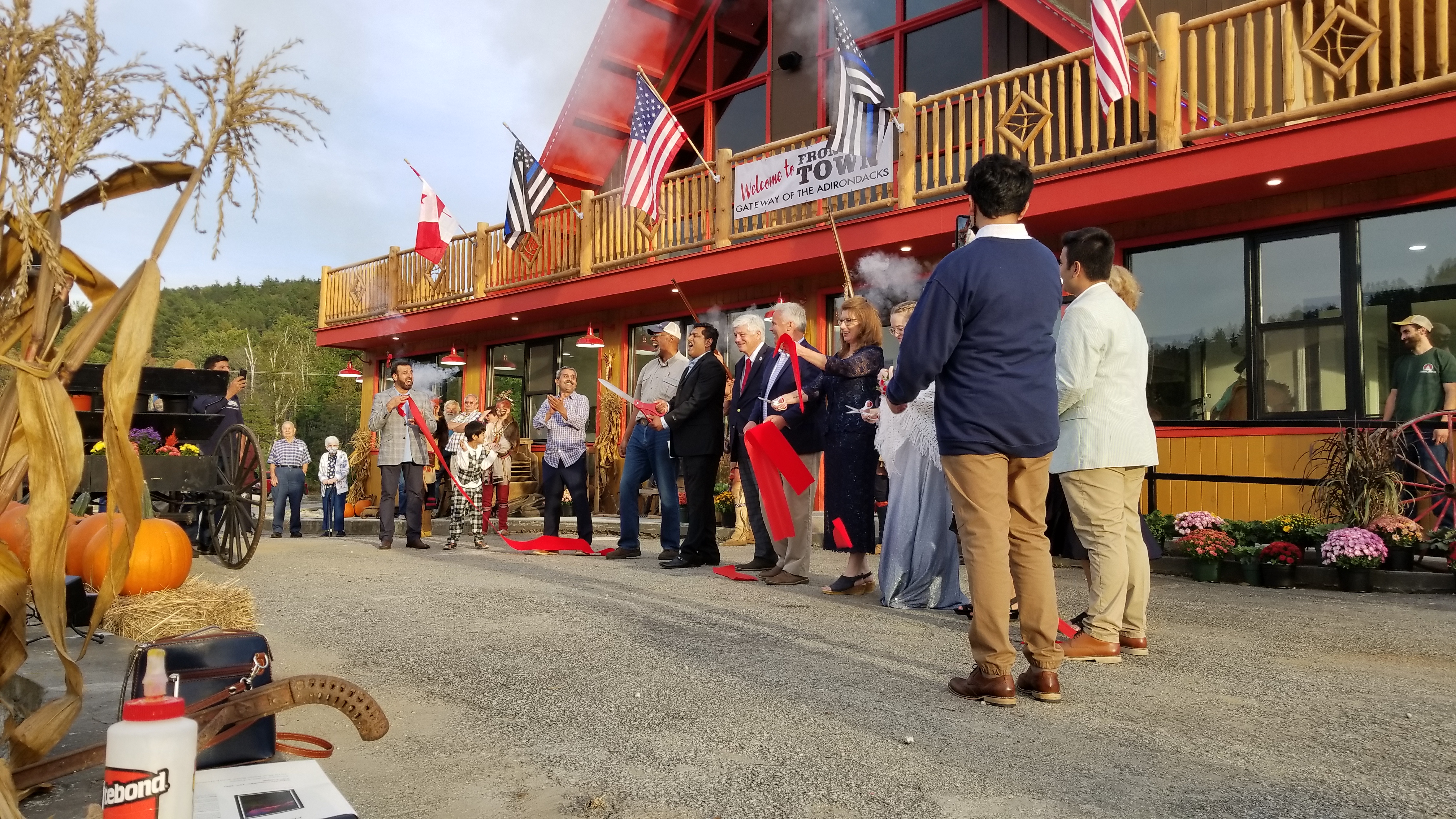 A line of people cut a red ribbon in front of a new, Adirondack-style building.