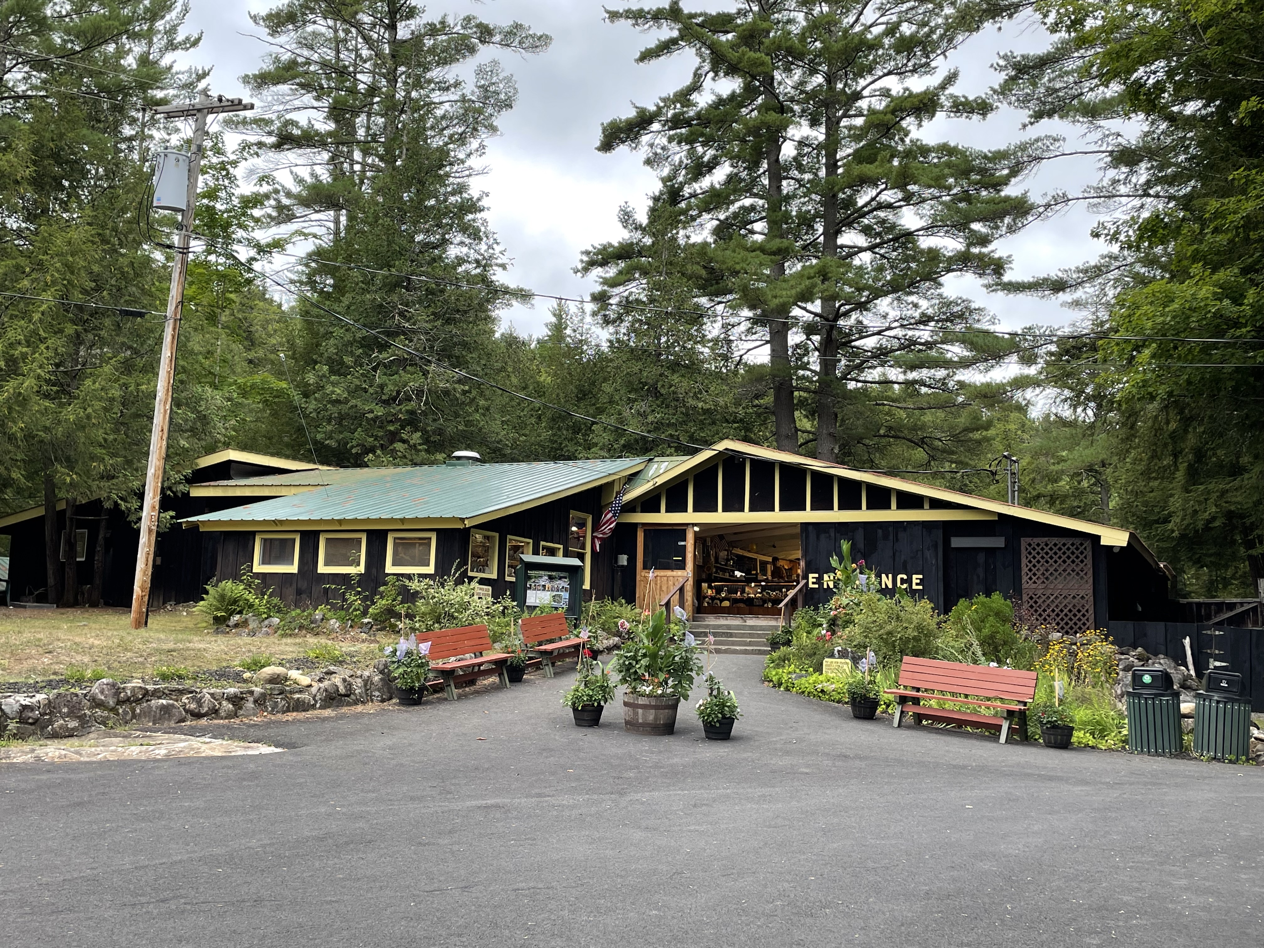 A one-story brown building with open doors is tucked into rocks and flowers. 