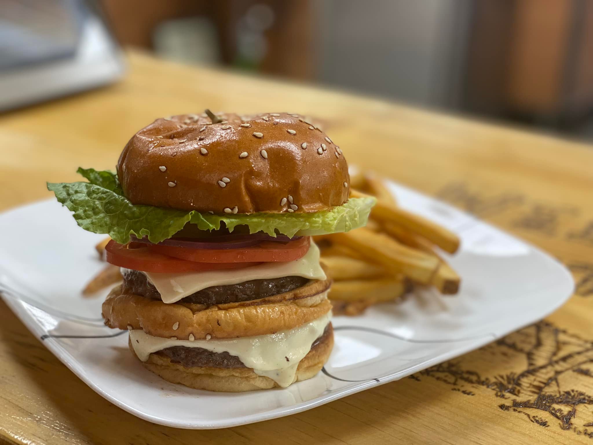 Close up of a tall, stacked cheeseburger on a rustic wooden table.