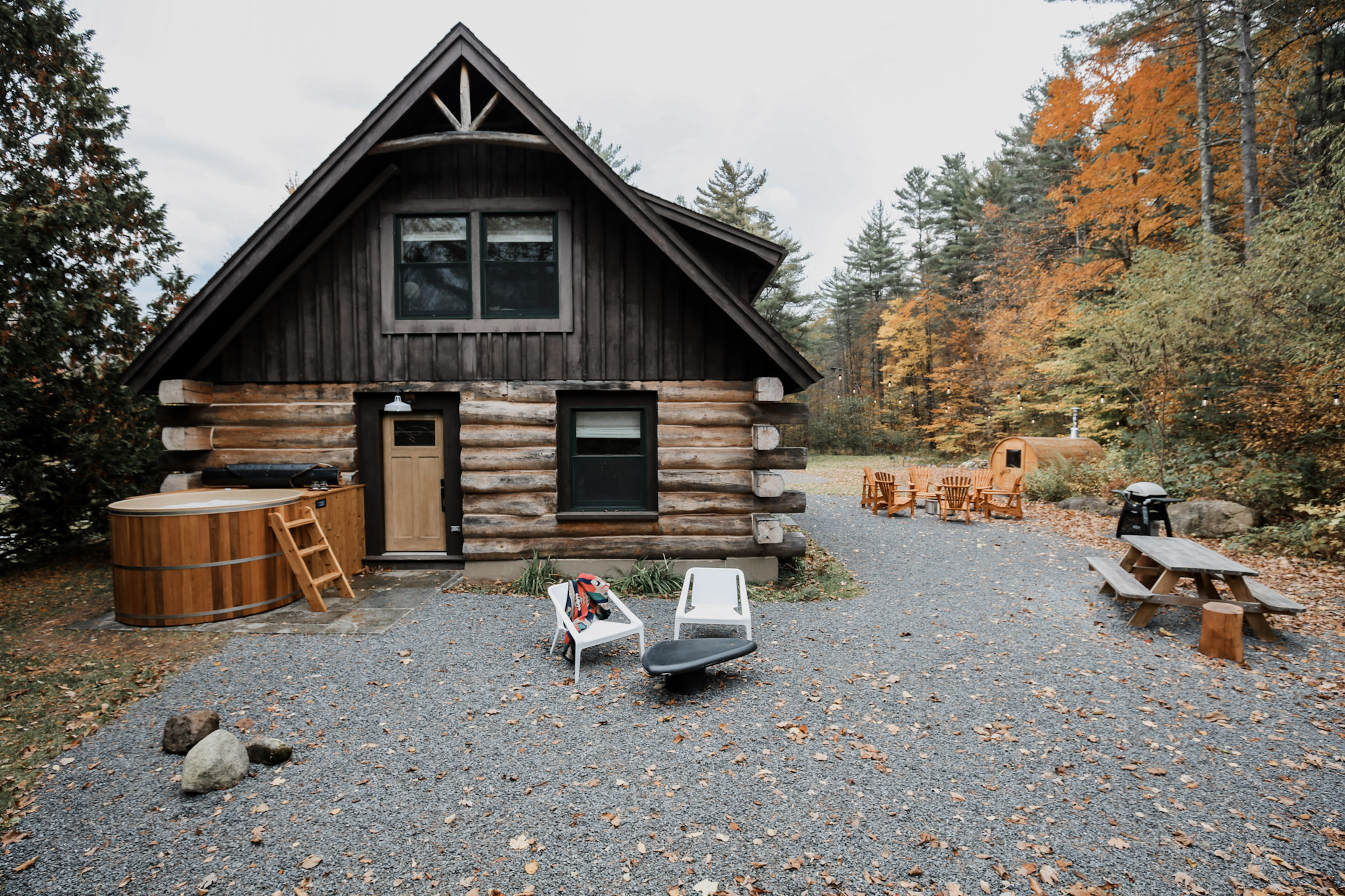 A log cabin with adirondack chairs and a sauna in the back.