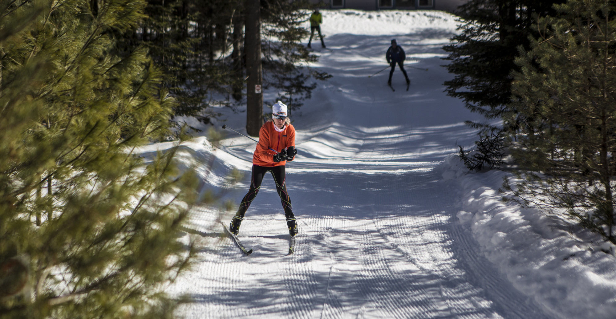 A woman and men cross country ski on a snowy trail. 