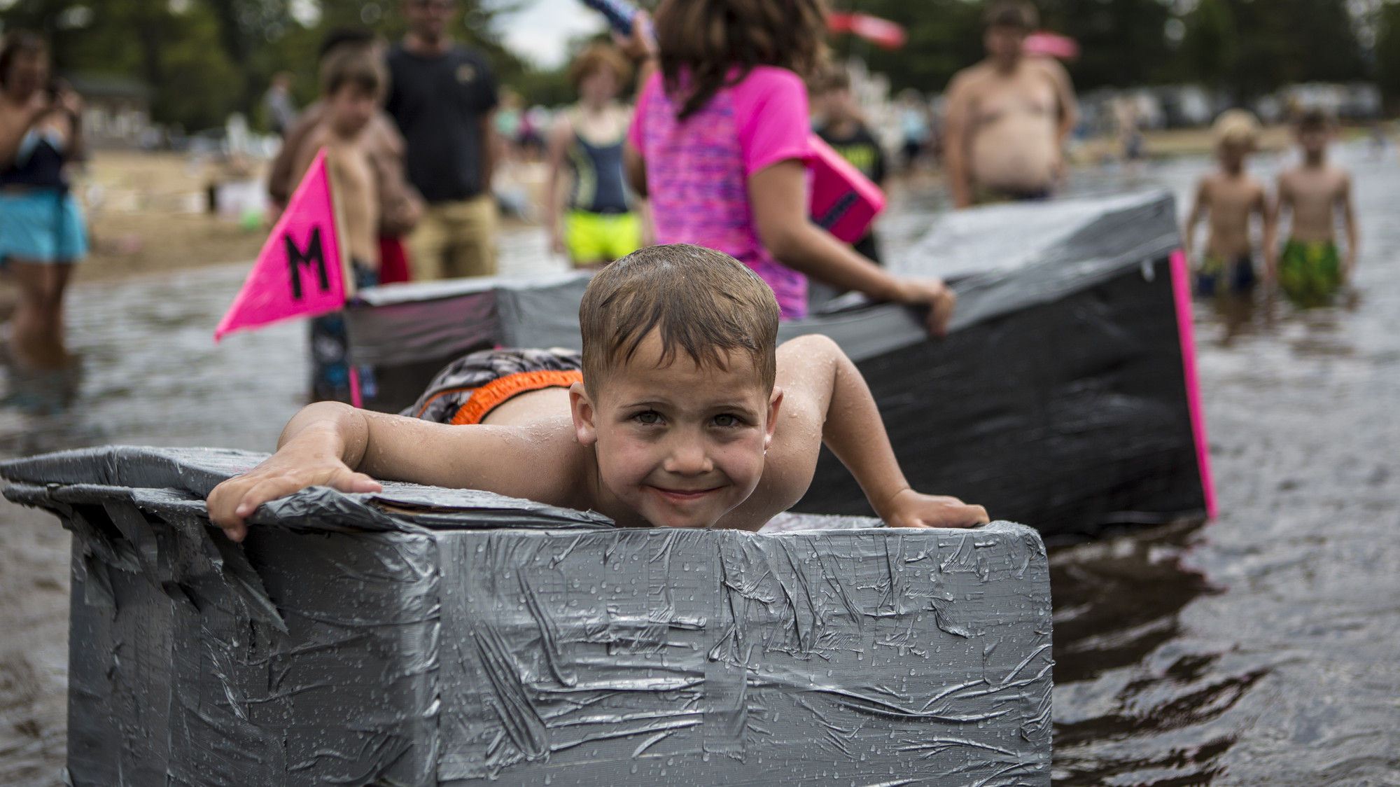 A child floats on a boat made of a duct tape-covered cardboard box.