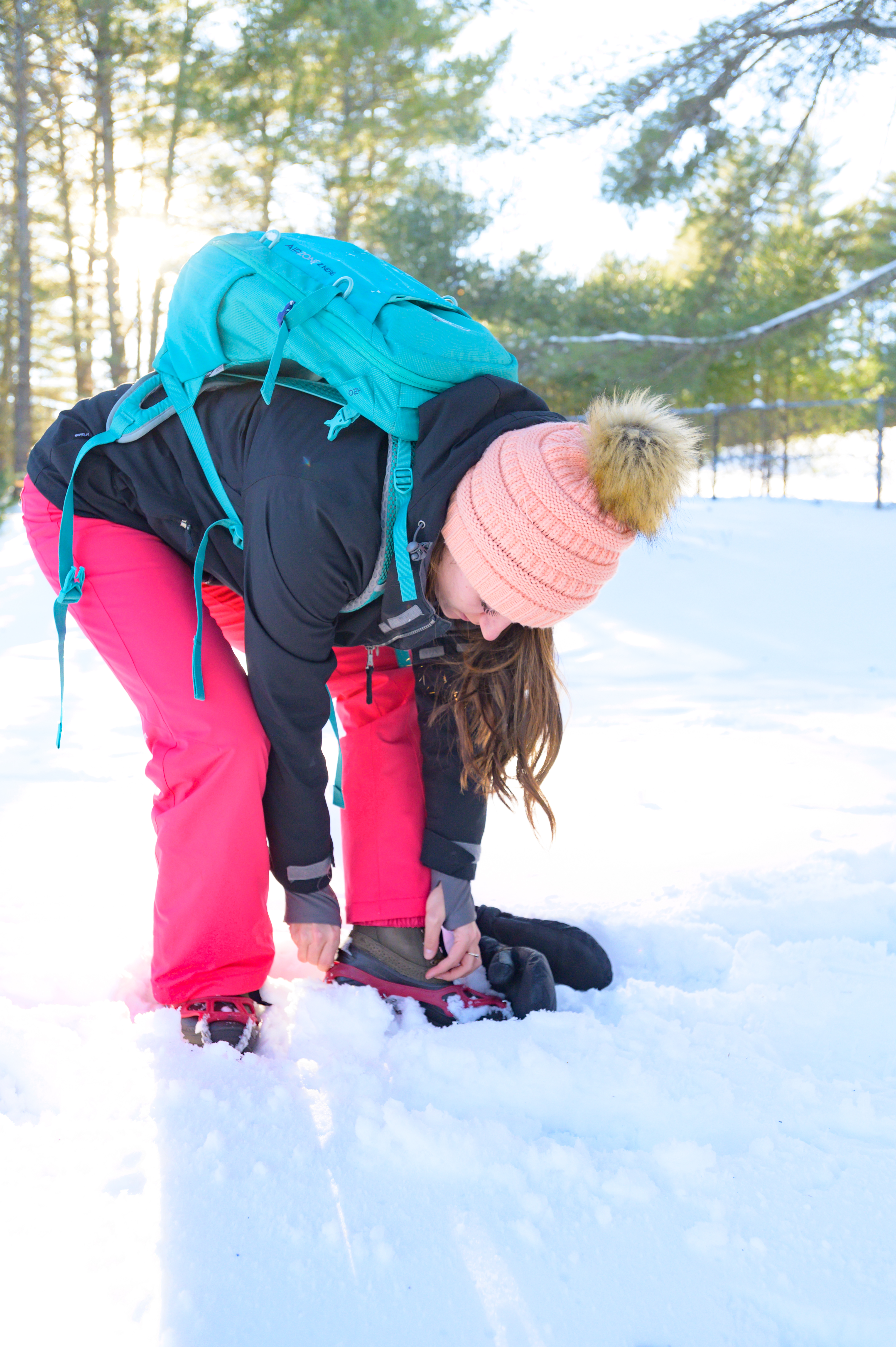 Woman putting on microspikes over boots in snow.