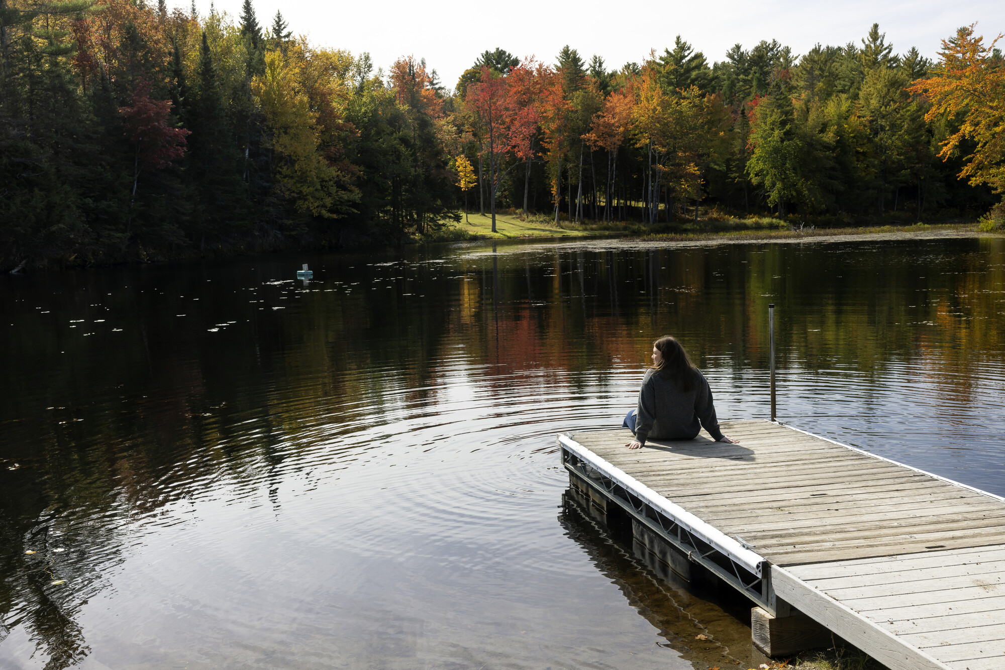 Woman sitting on a dock with fall trees on the shore line.