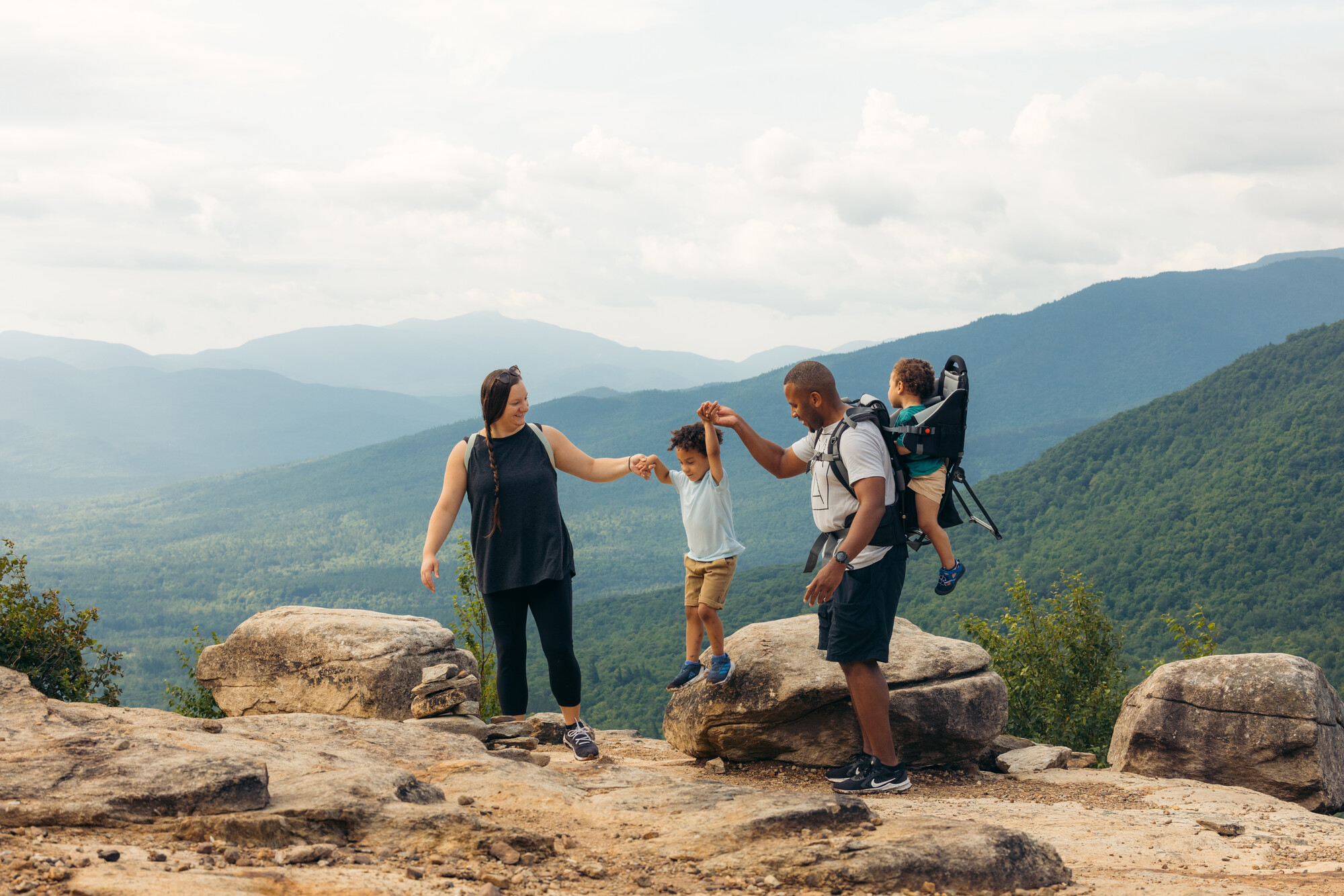 Mother and father hold hands of young boy jumping from rock