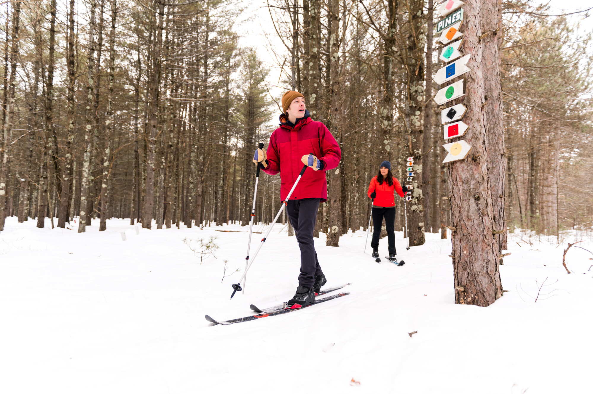 A man and a woman reach an intersection in the cross country ski trails, indicated by numerous signs designating different paths they could choose.