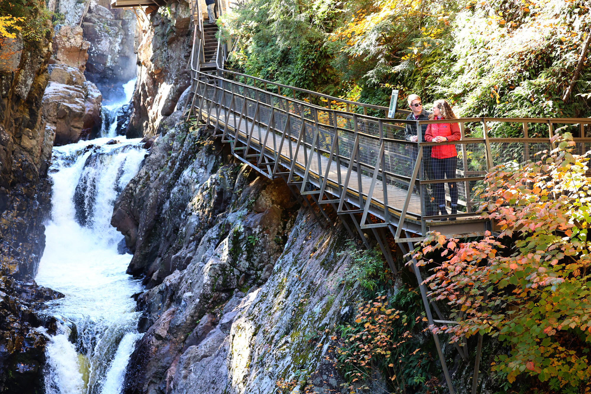 Couple stands on walking path at High Falls Gorge with waterfalls surrounding them.