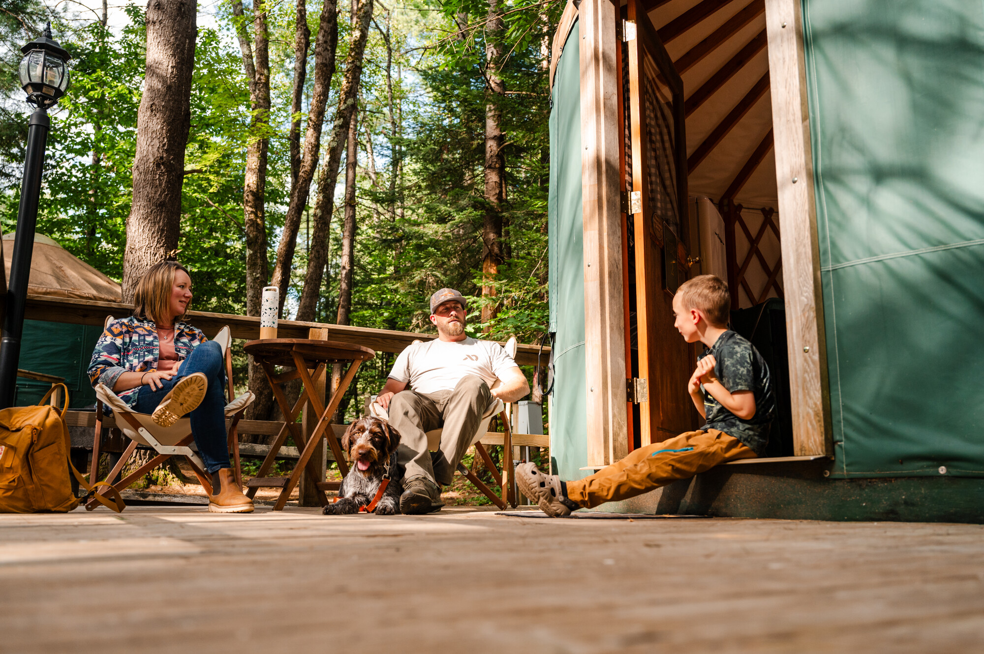A man and woman sit on the front porch of a yurt with a young boy. 