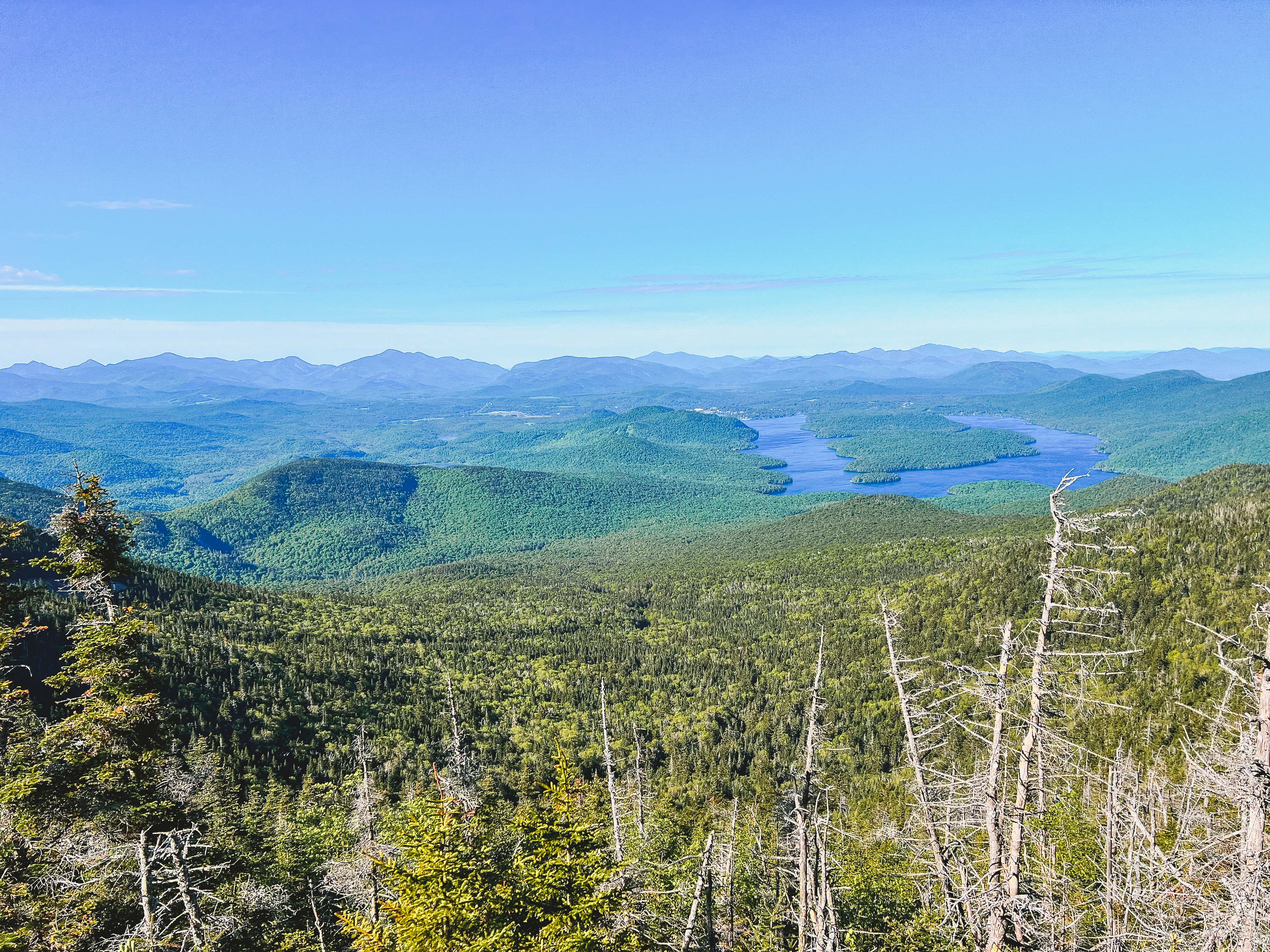 A view from a mountain in summer with a horseshoe shaped lake and more mountains in the distance.