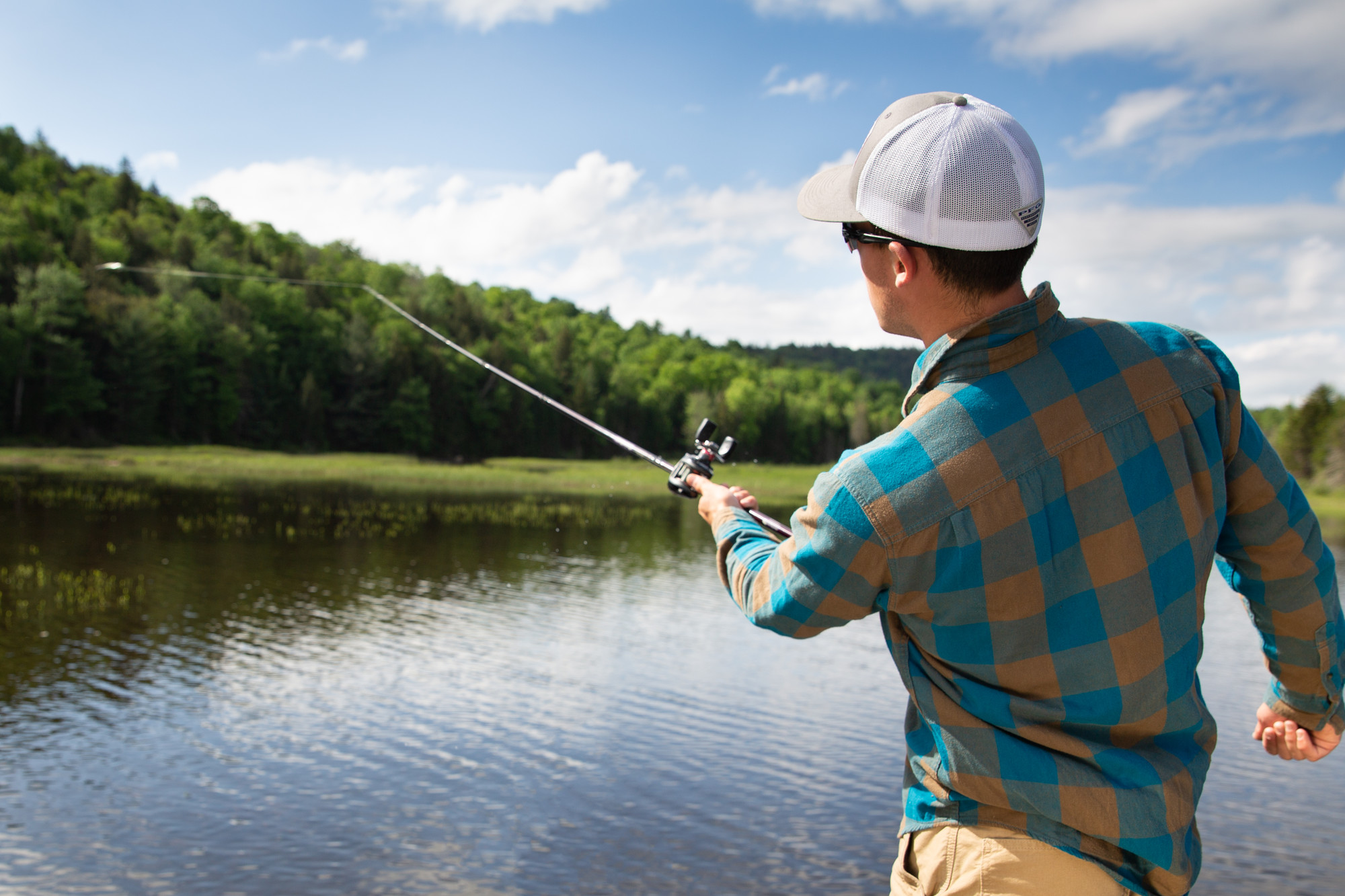 A man wearing a flannel shirt casts a fishing pole left-handed into the waters of Big Tupper Lake