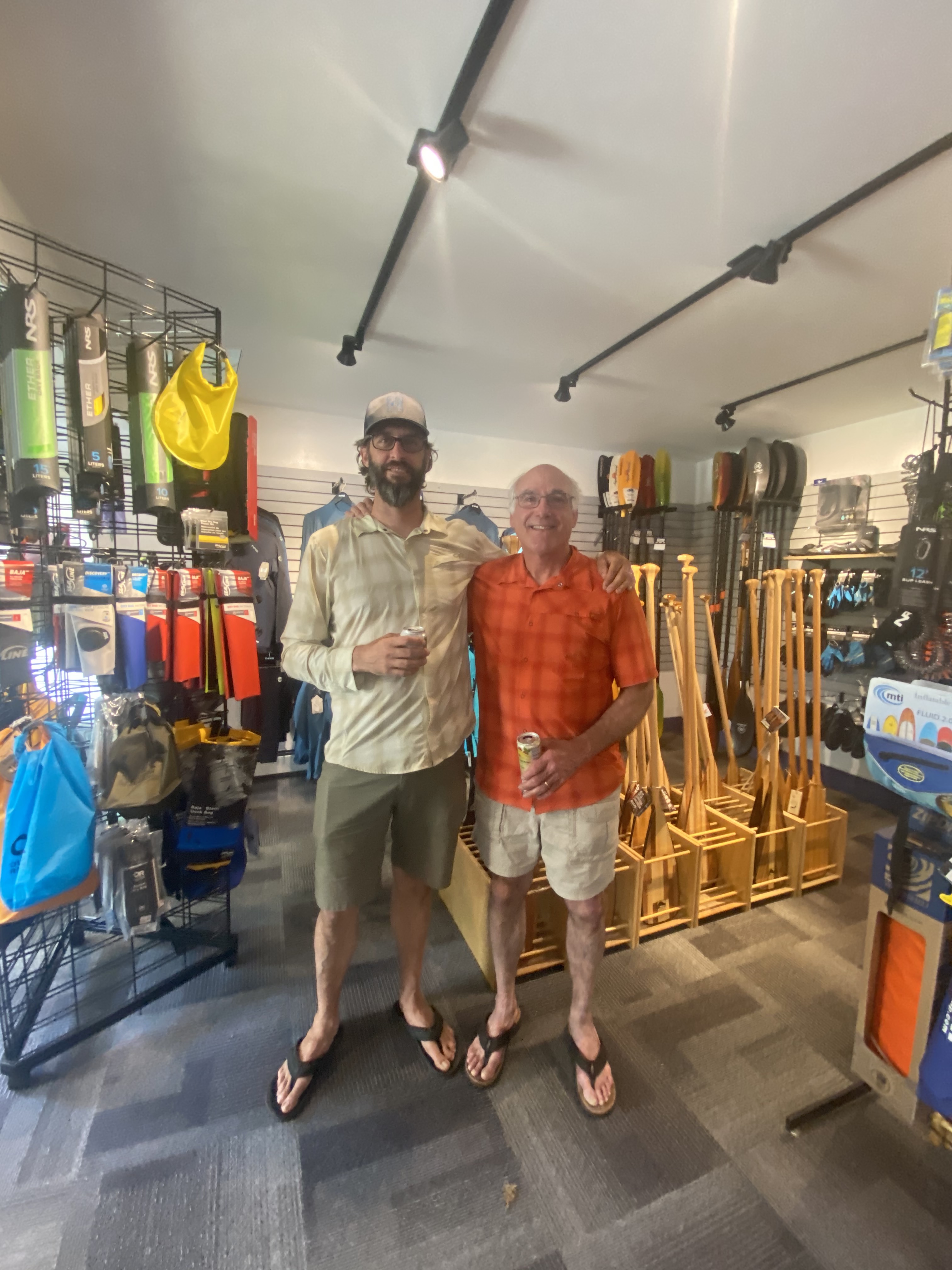 Jason Smith and Steve Doxzon stand inside Adirondack Lakes and Trails Outfitters Two men stand inside a store in front of paddle gear