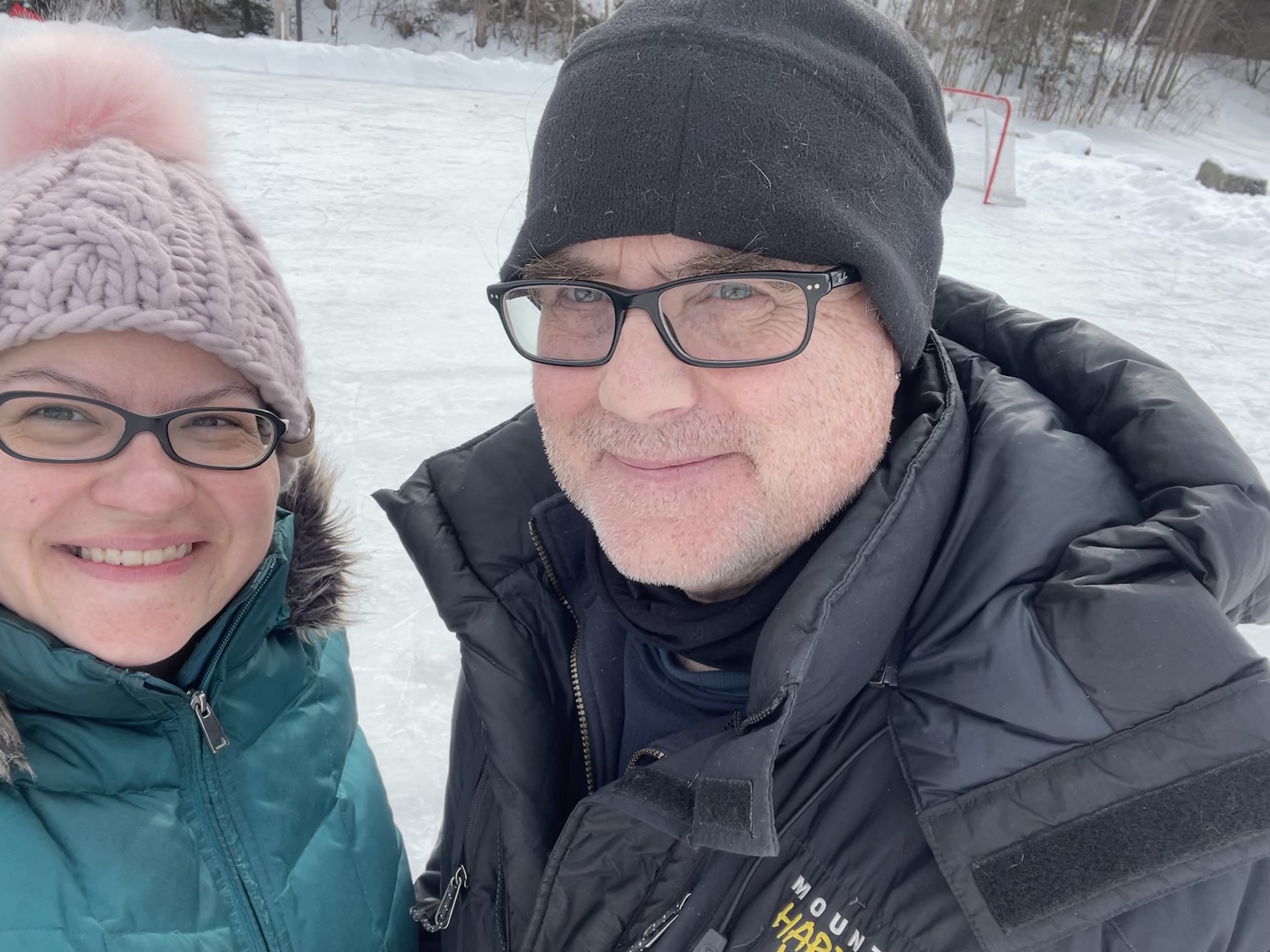 A man and woman in winter coats and hats on an outdoor skating rink.