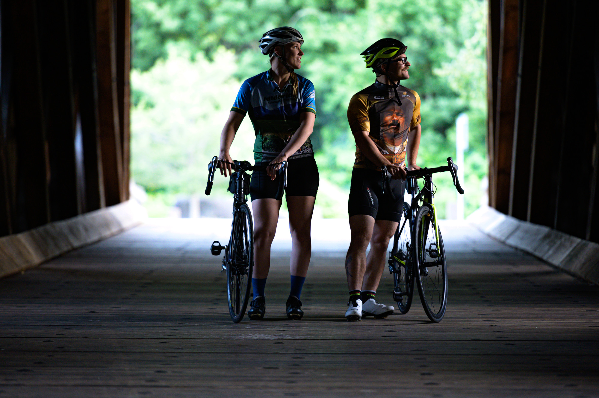 A man and woman walk their bicycles on a covered bridge. 