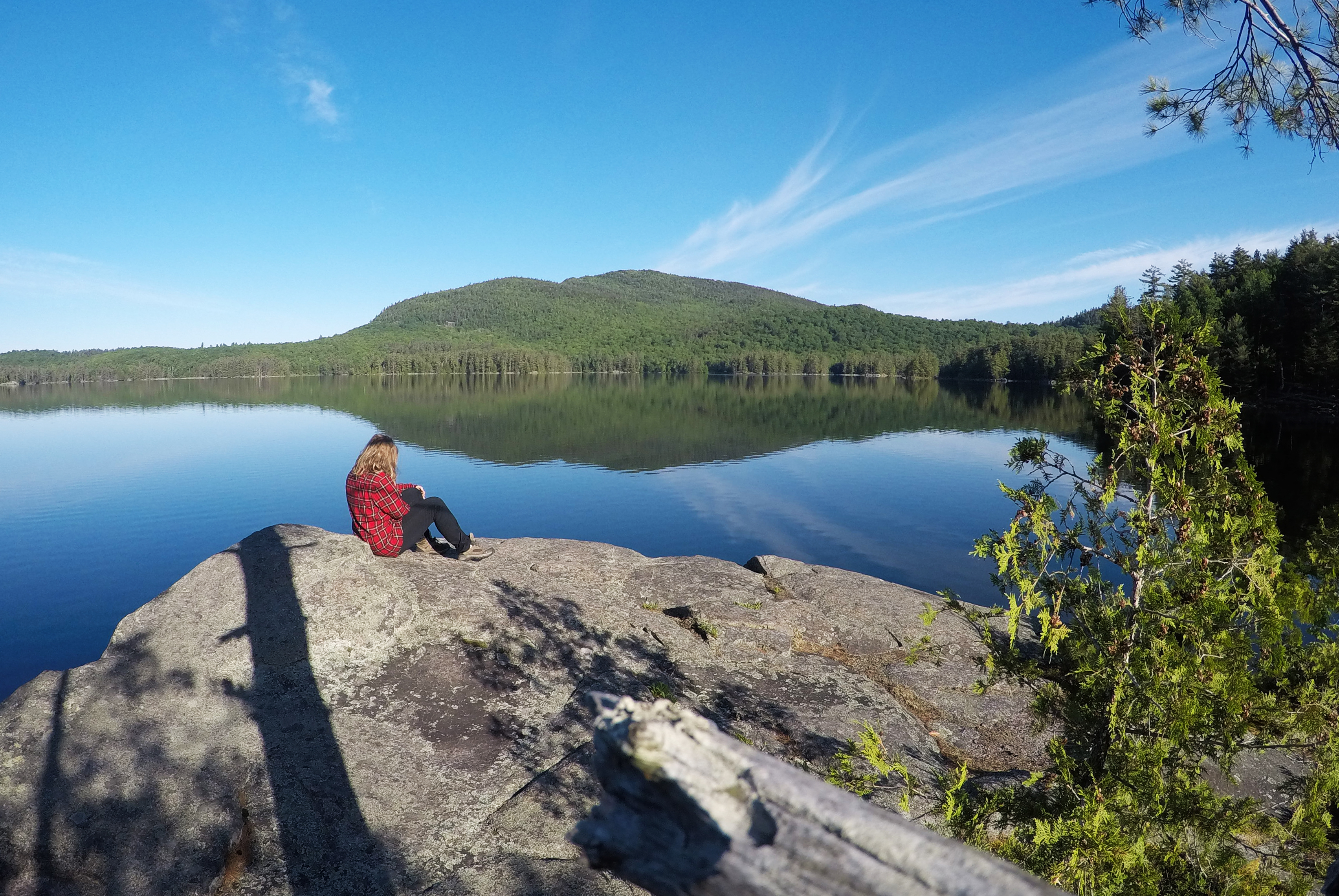 A hiker sits on the shore of a lake with one mountain rising on the opposite shore.