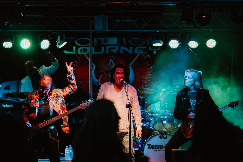 A group of three older men perform rock music under bright stage lights with green fog. 