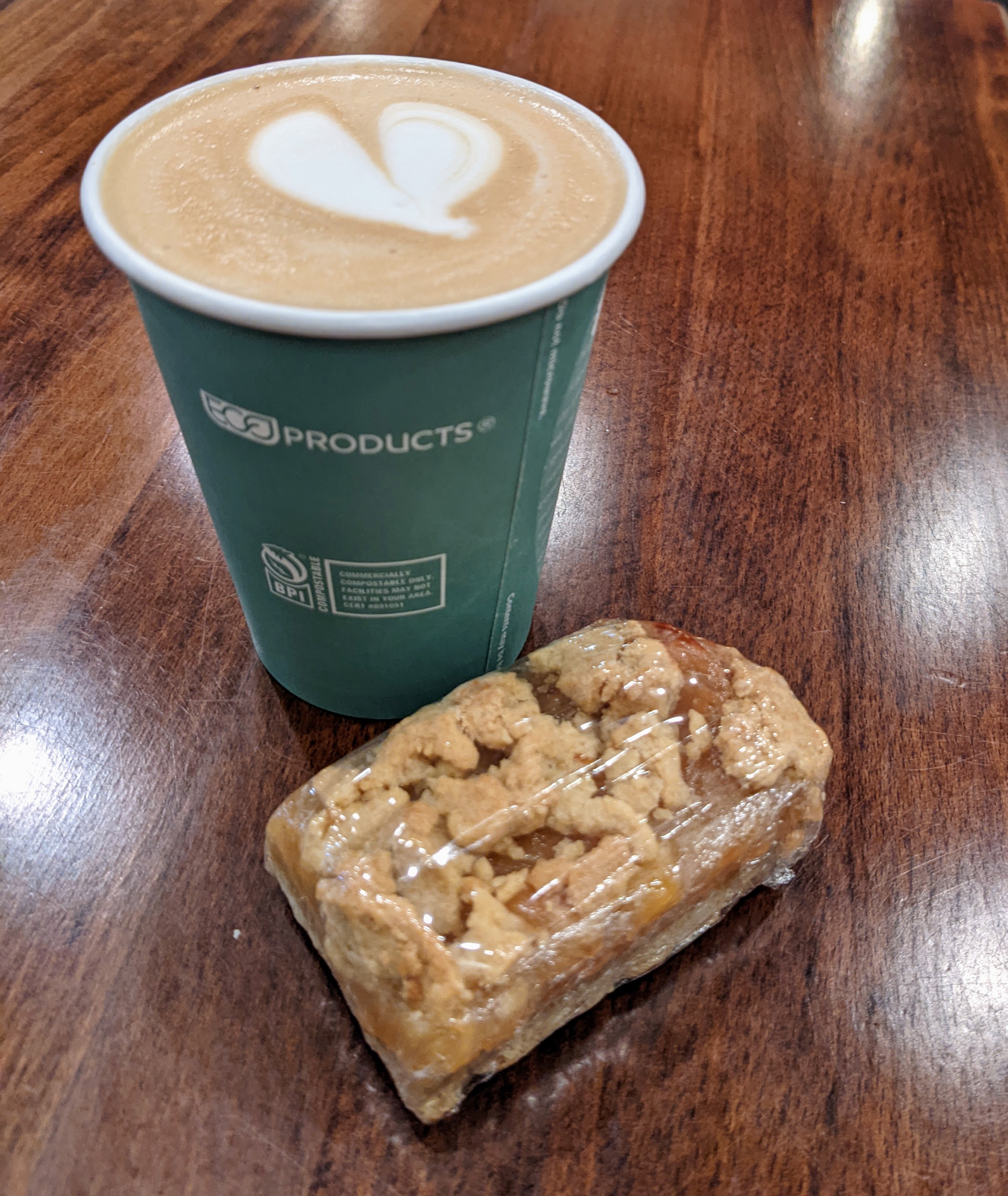 A wooden table holds a baked apple bar and a warm, vanilla latte with a heart drawn with the foam