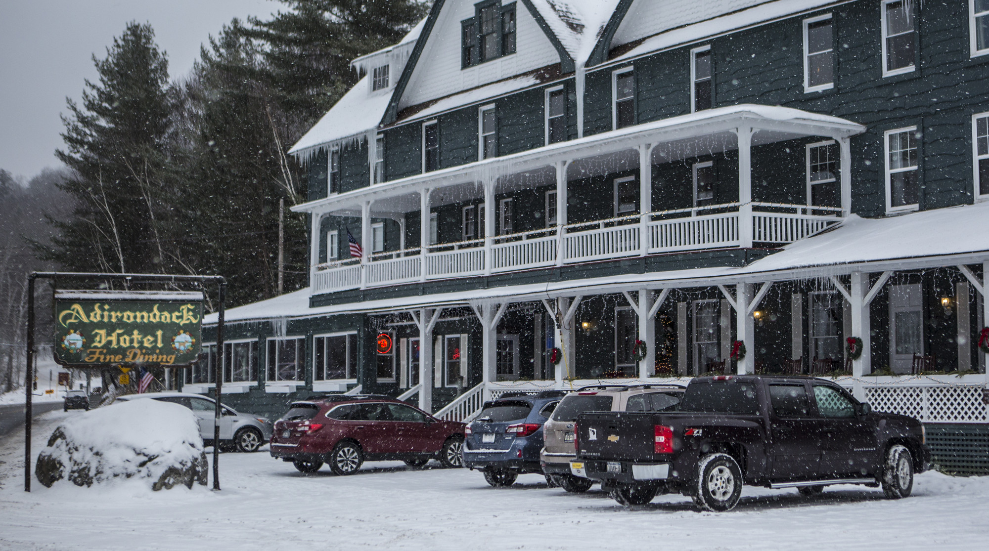 An old style hotel in winter with cars parked out front. 
