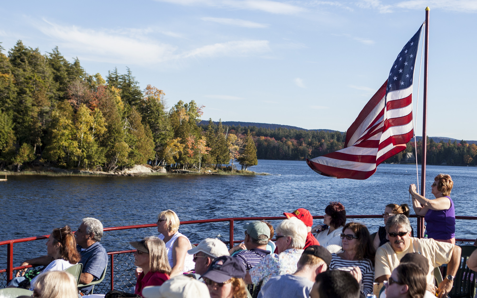 Top deck of a boat filled with people enjoying the view of the water and shore