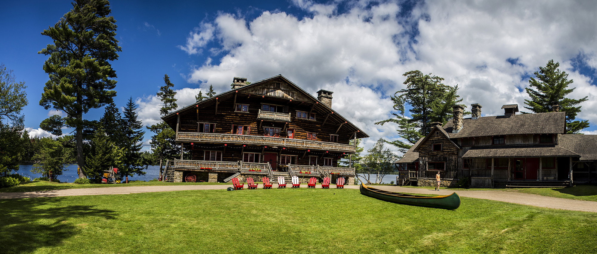 The rustic main lodge of Great Camp Sagamore with red Adirondack chair out front.