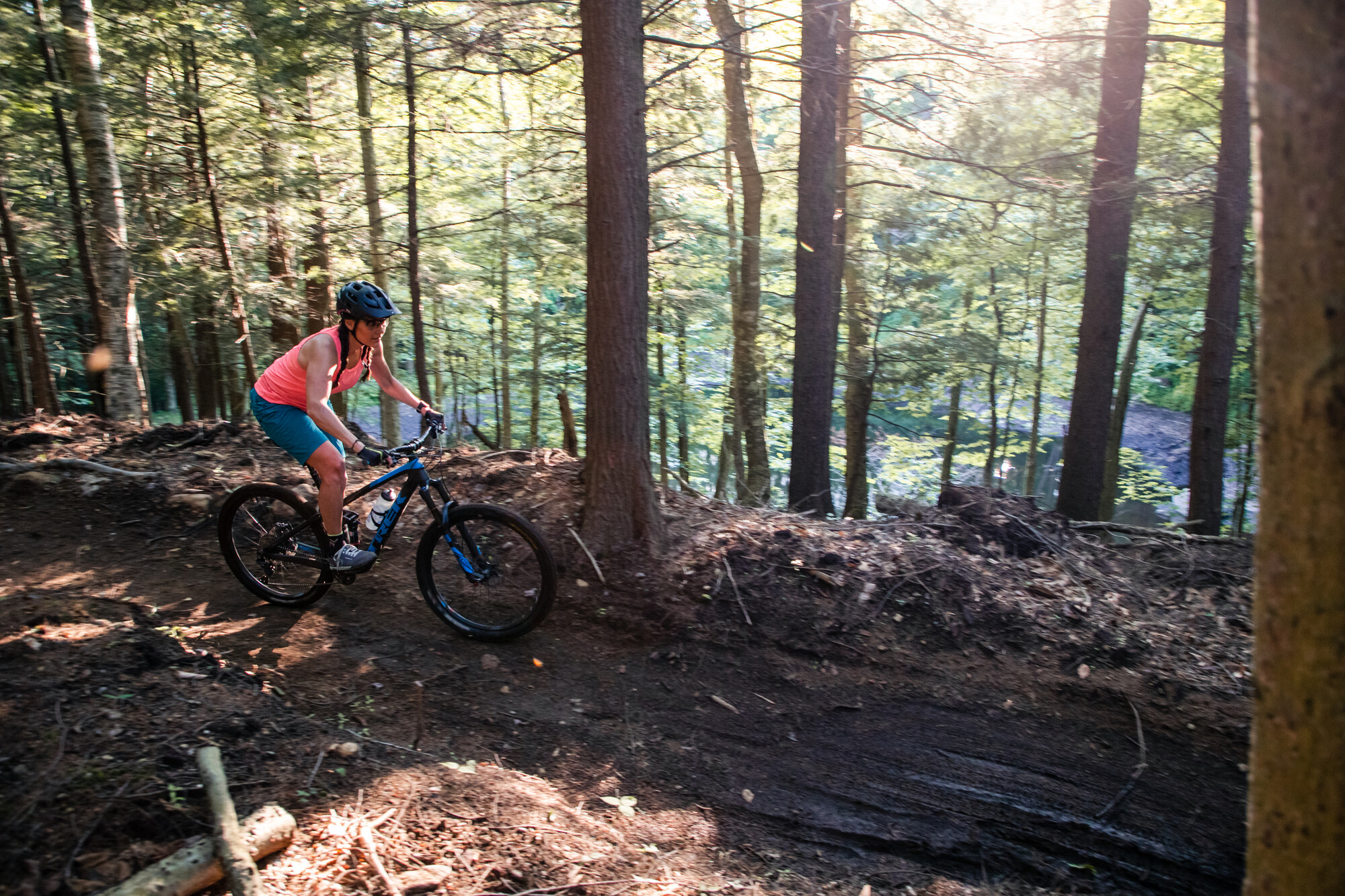 A woman rides a mountain bike down a dirt trail through the forest.