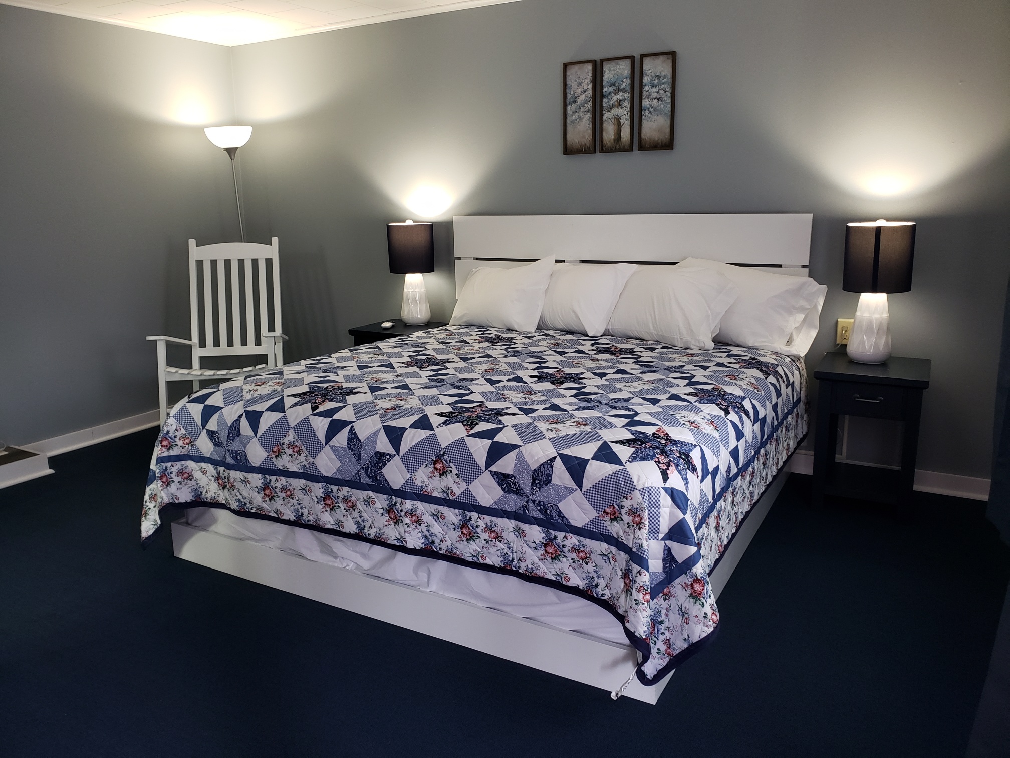 A cheerful, clean motel room featuring a colorful quilt and Adirondack rocking chair.