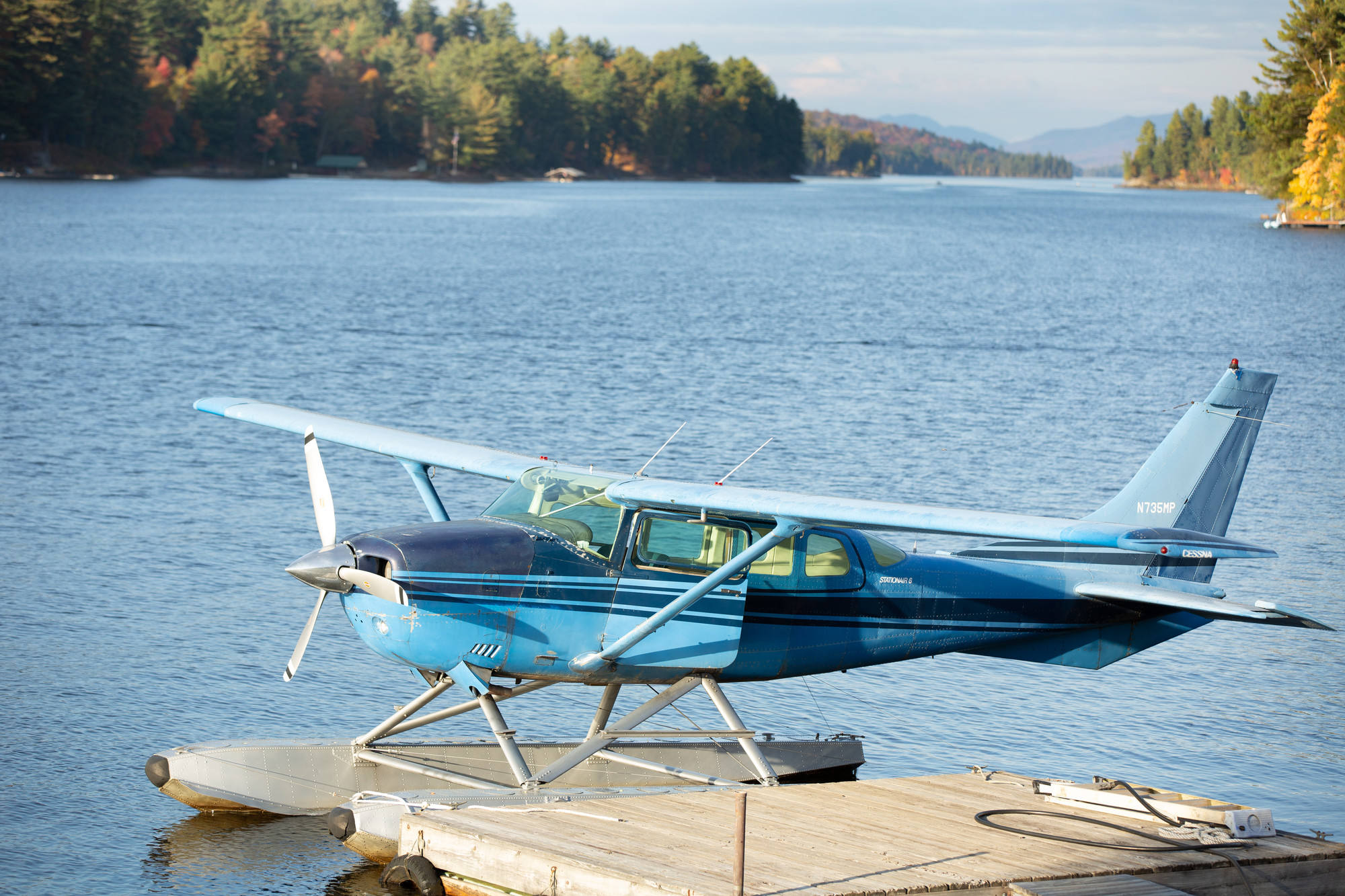 A float plane at a dock on a lake mountains and tree-lined shore beyond.