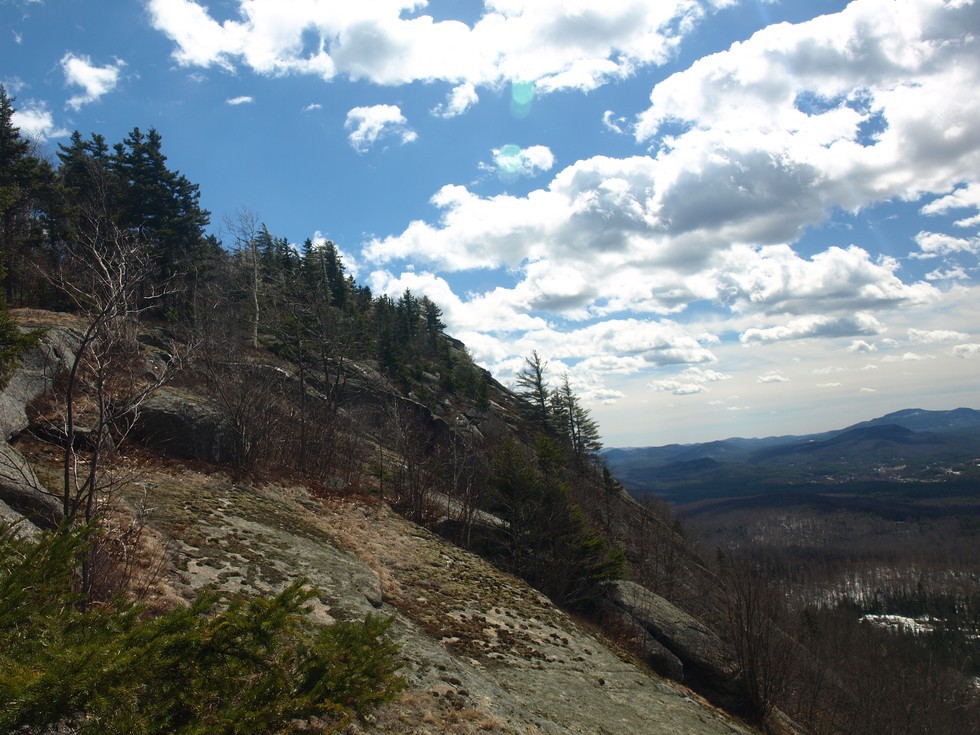 Looking outward from a mountain ride, with sloping rocks on the left and views of other mountains to the right.
